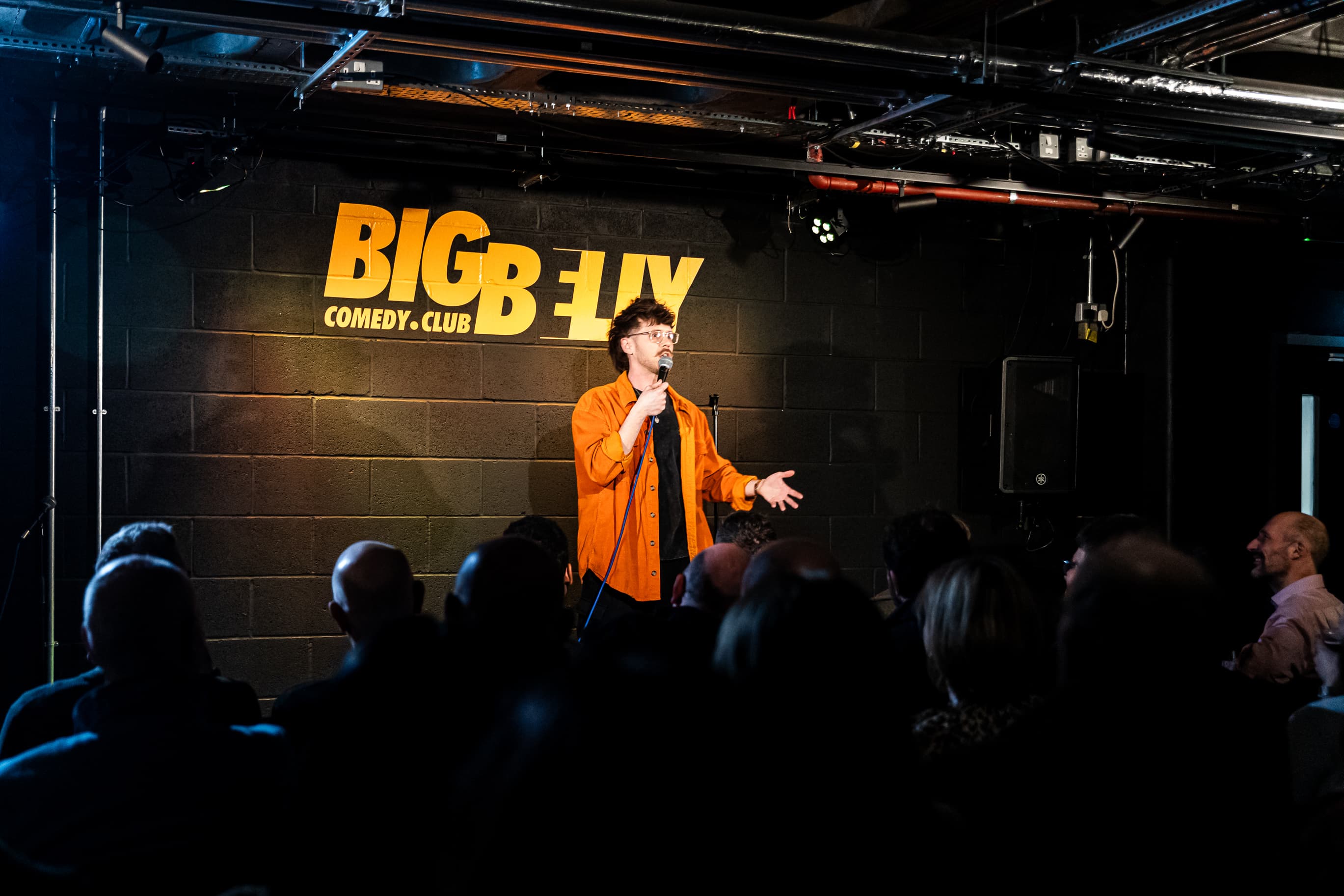 Solo comedian on stage at Big Belly Comedy Club, intimate brickwork venue for live stand-up events.