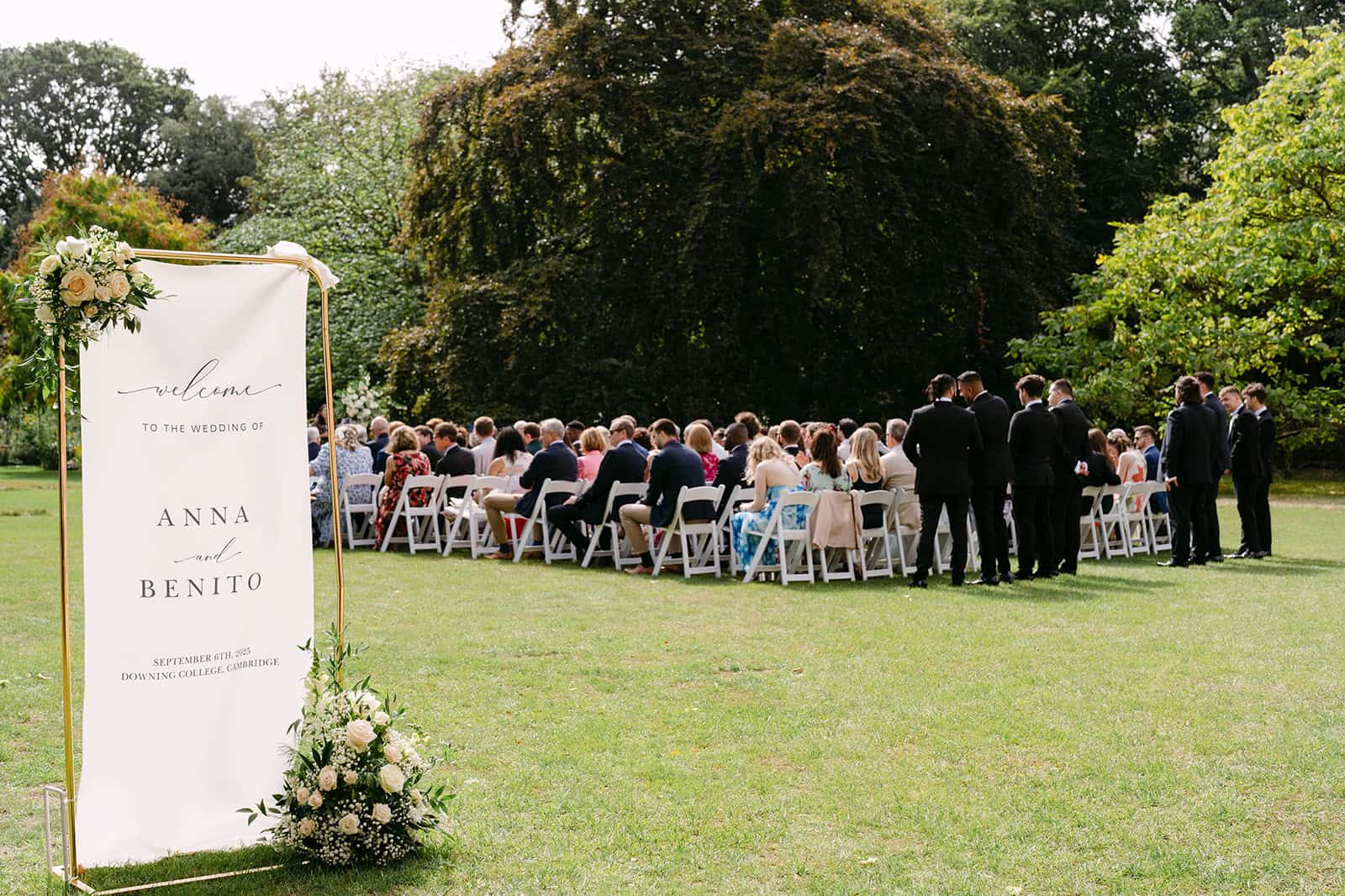 Outdoor ceremony in Fellows' Garden with white chairs and welcome sign for wedding event venue.