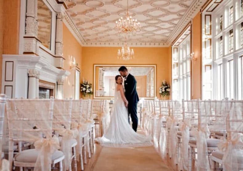Gold Room wedding ceremony at Holmewood Hall with ornate architecture and elegant Chiavari chairs.