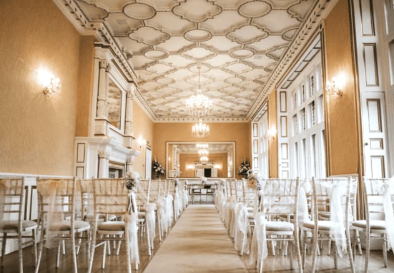 Gold Room at Holmewood Hall: elegant ceremony venue with ornate plasterwork and aisle seating.