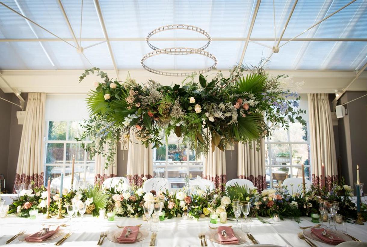 Luxury Lake Suite dining table with overhead floral installation for elegant garden weddings.