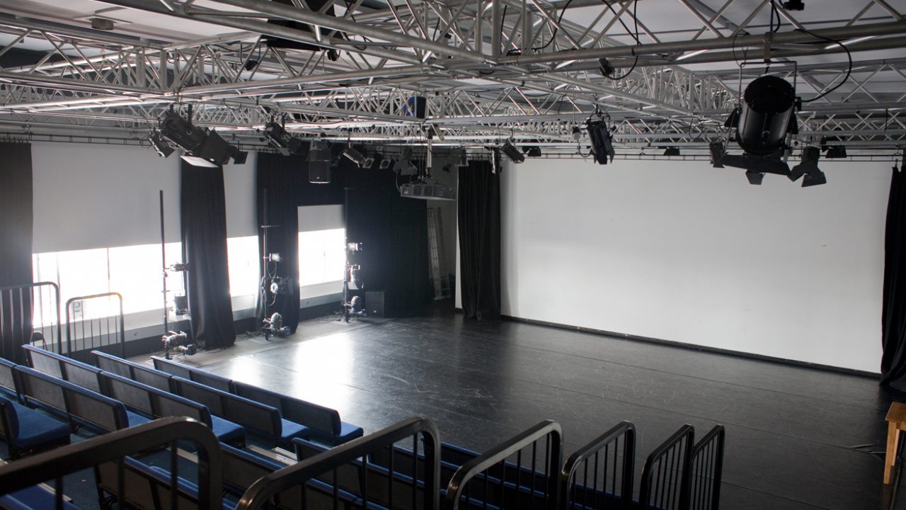 Black-box theatre studio with tiered seating and lighting grid for presentations and workshops.
