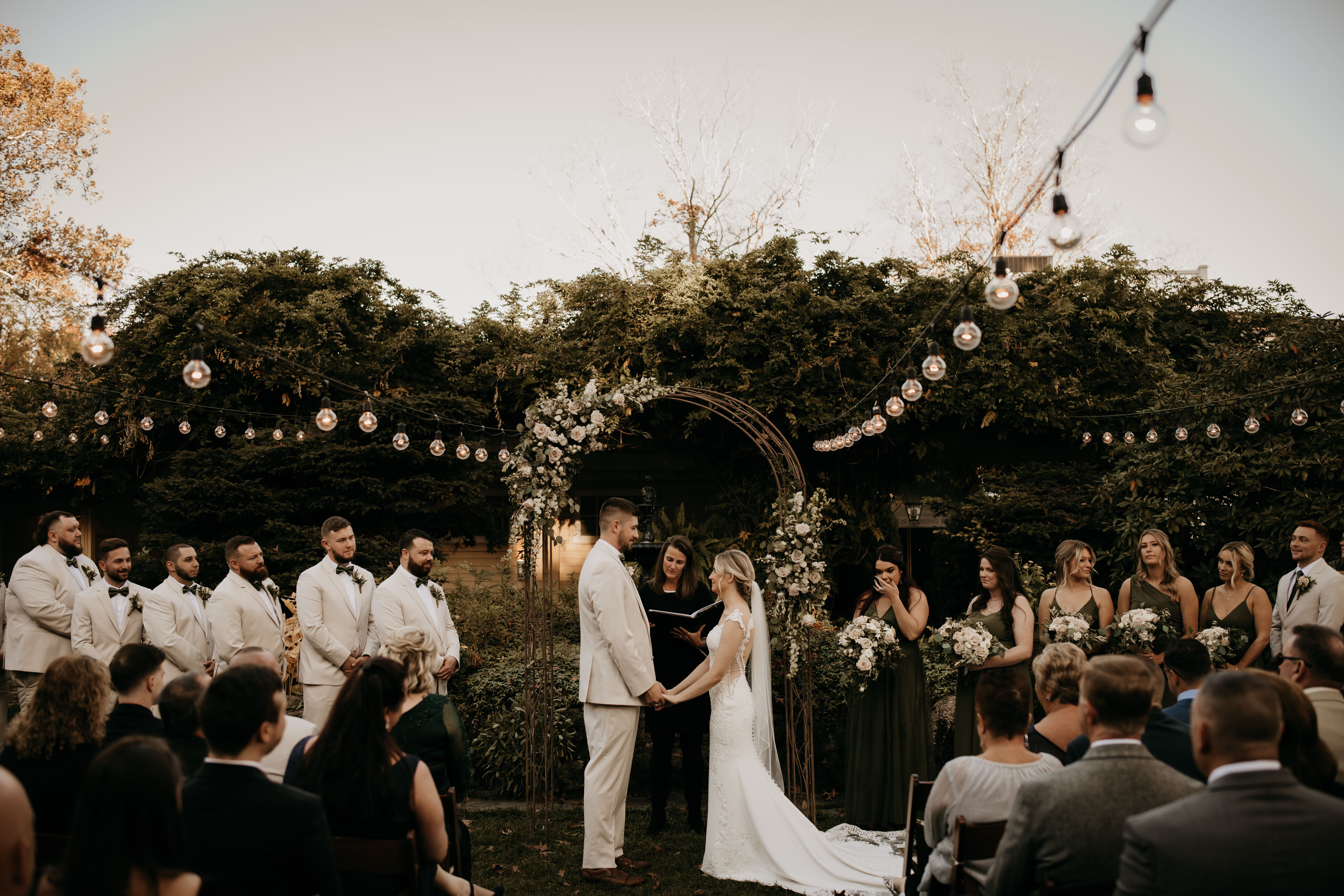 Outdoor wedding ceremony at The New Chichester Hotel with bistro lighting and foliage backdrop.