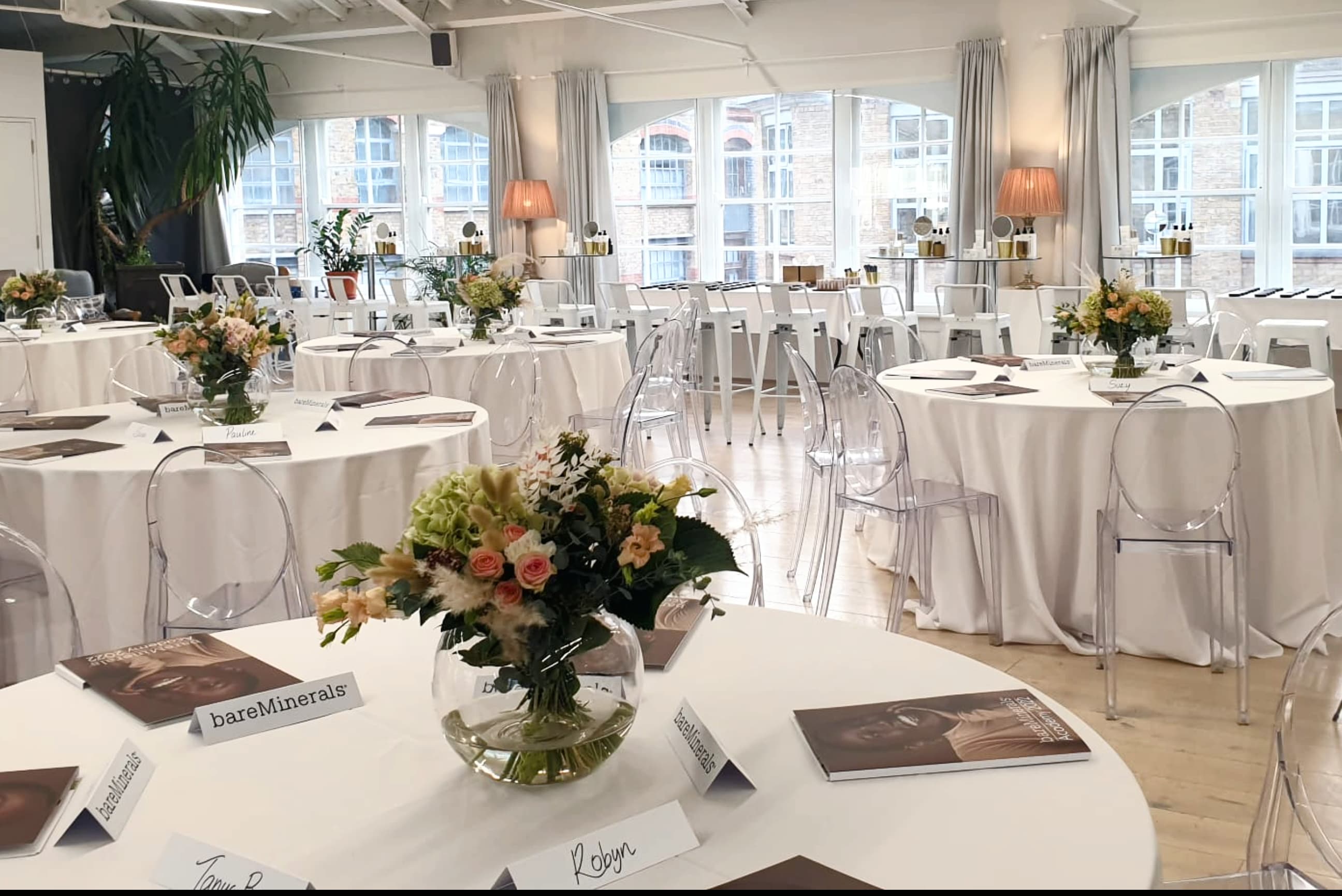 Modern event space with ghost chairs and floral decor for corporate luncheon or product showcase.