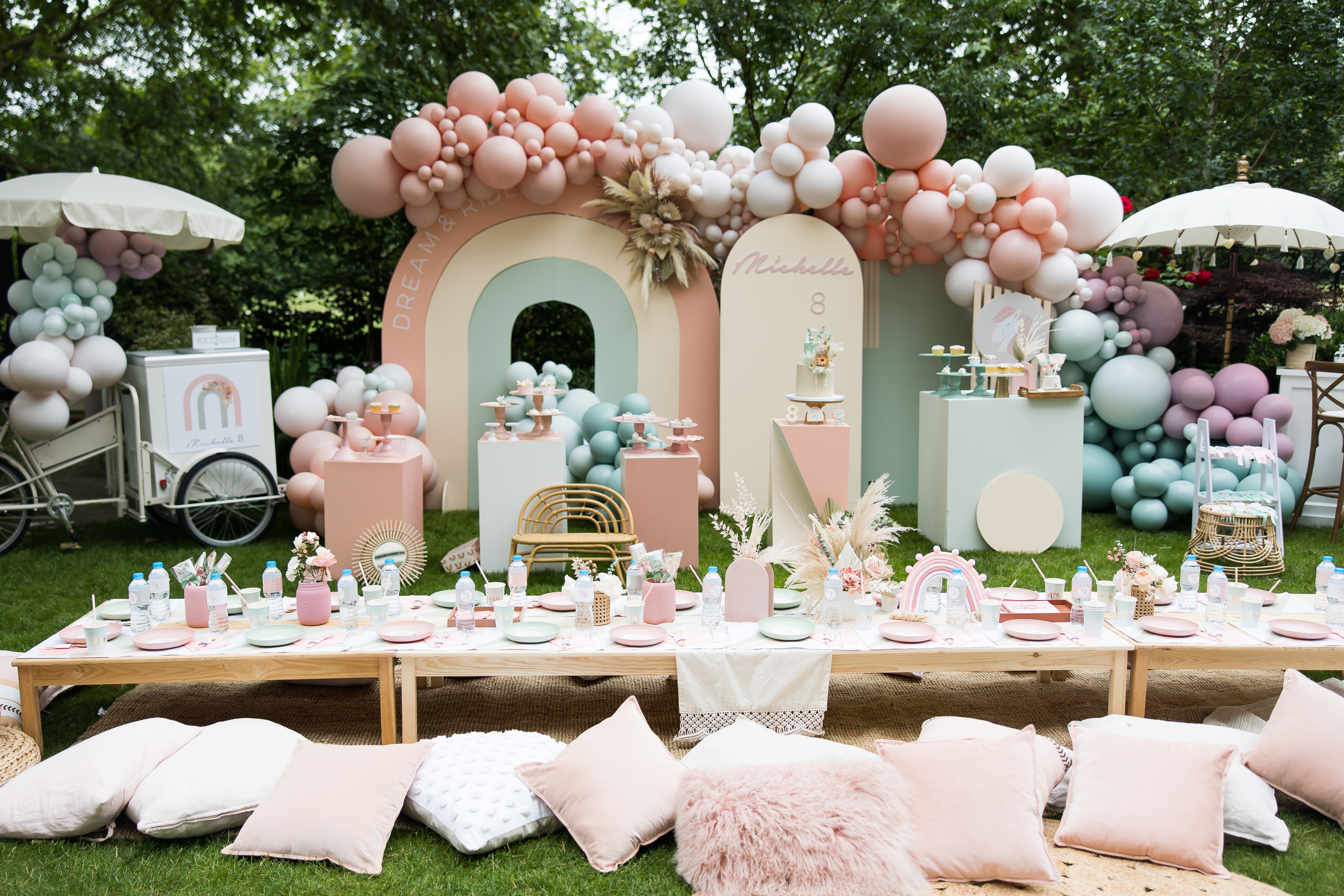 Elegant outdoor event setup with pastel balloon arch for birthday or baby shower.