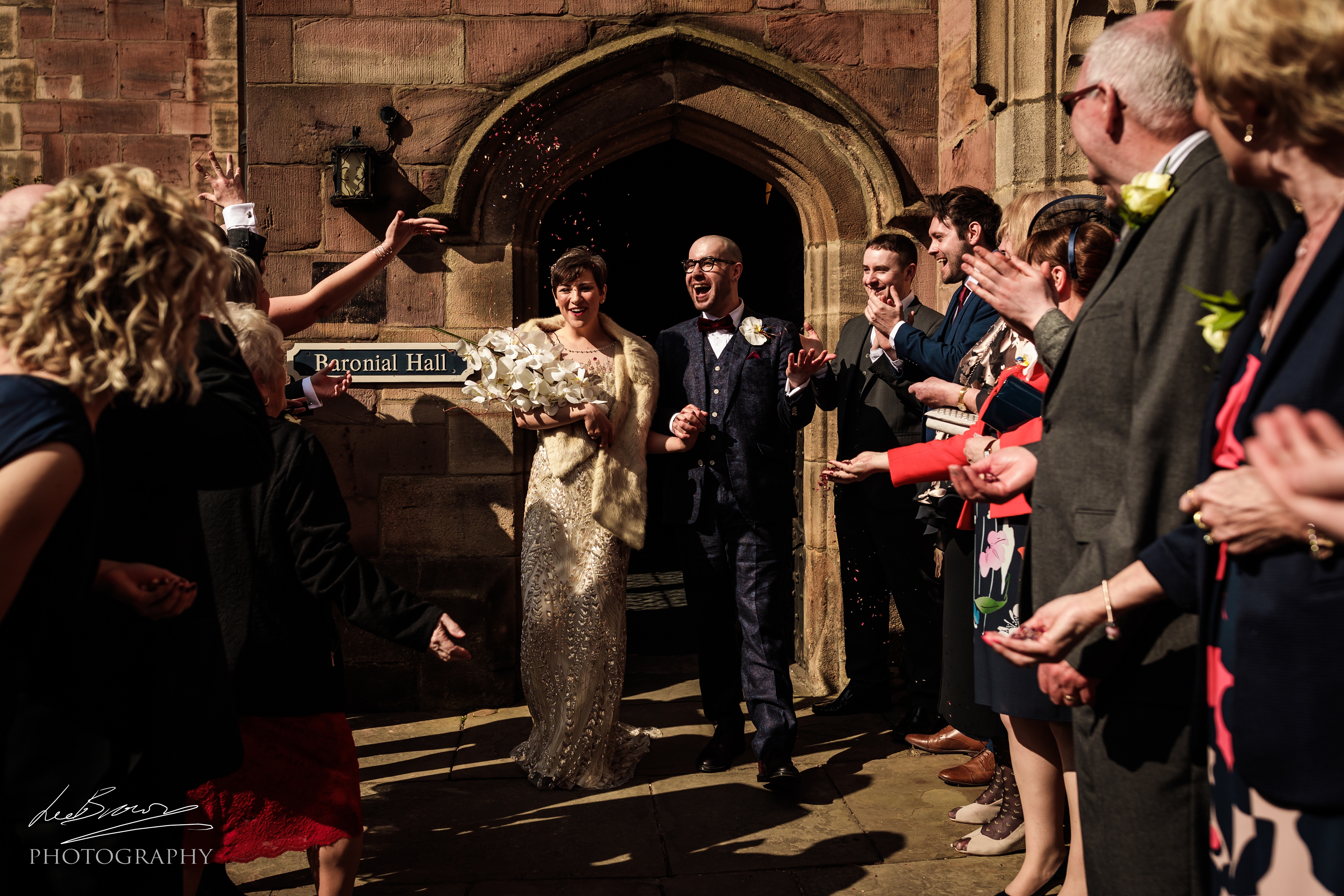 Joyful couple exiting Baronial Hall, Chetham's Library, celebrating a wedding with confetti.