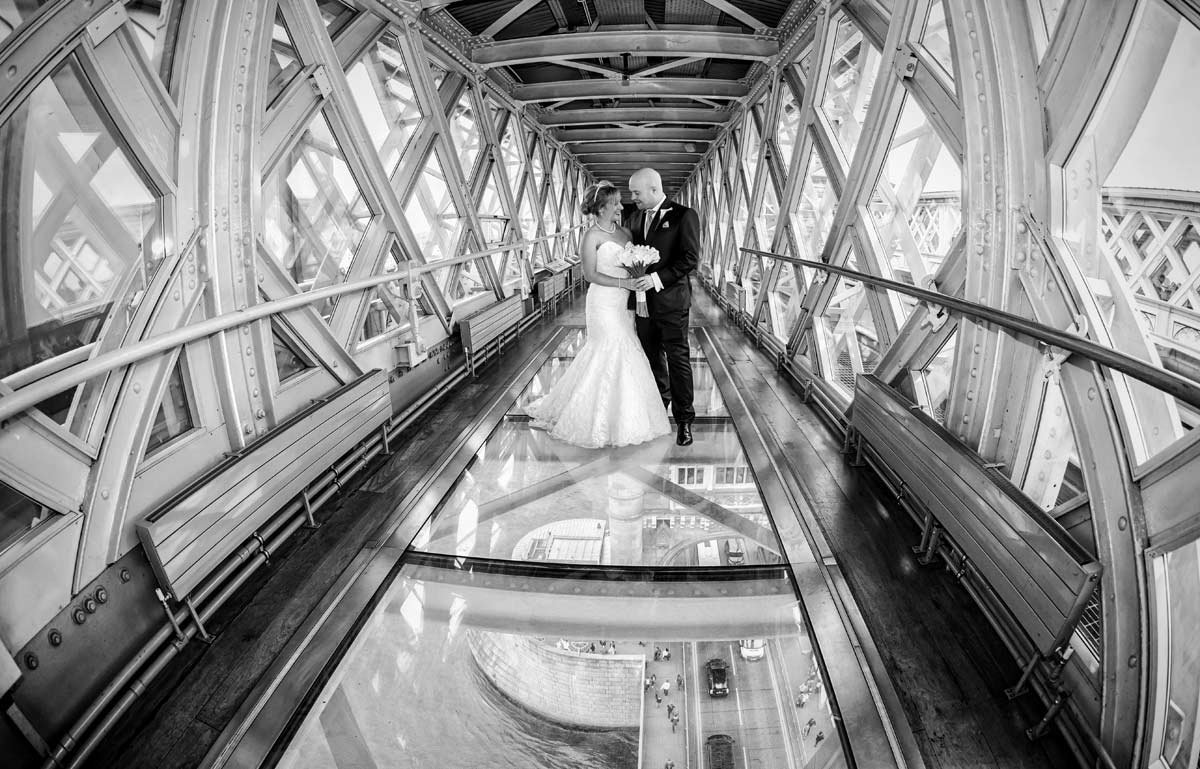 Couple in wedding attire on glass walkway at Tower Bridge, perfect for elegant events.