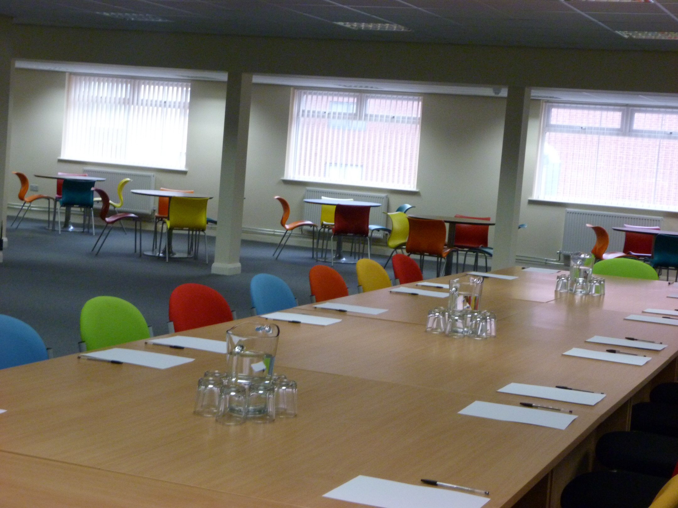 Versatile training room with long table and colorful chairs for meetings and workshops.