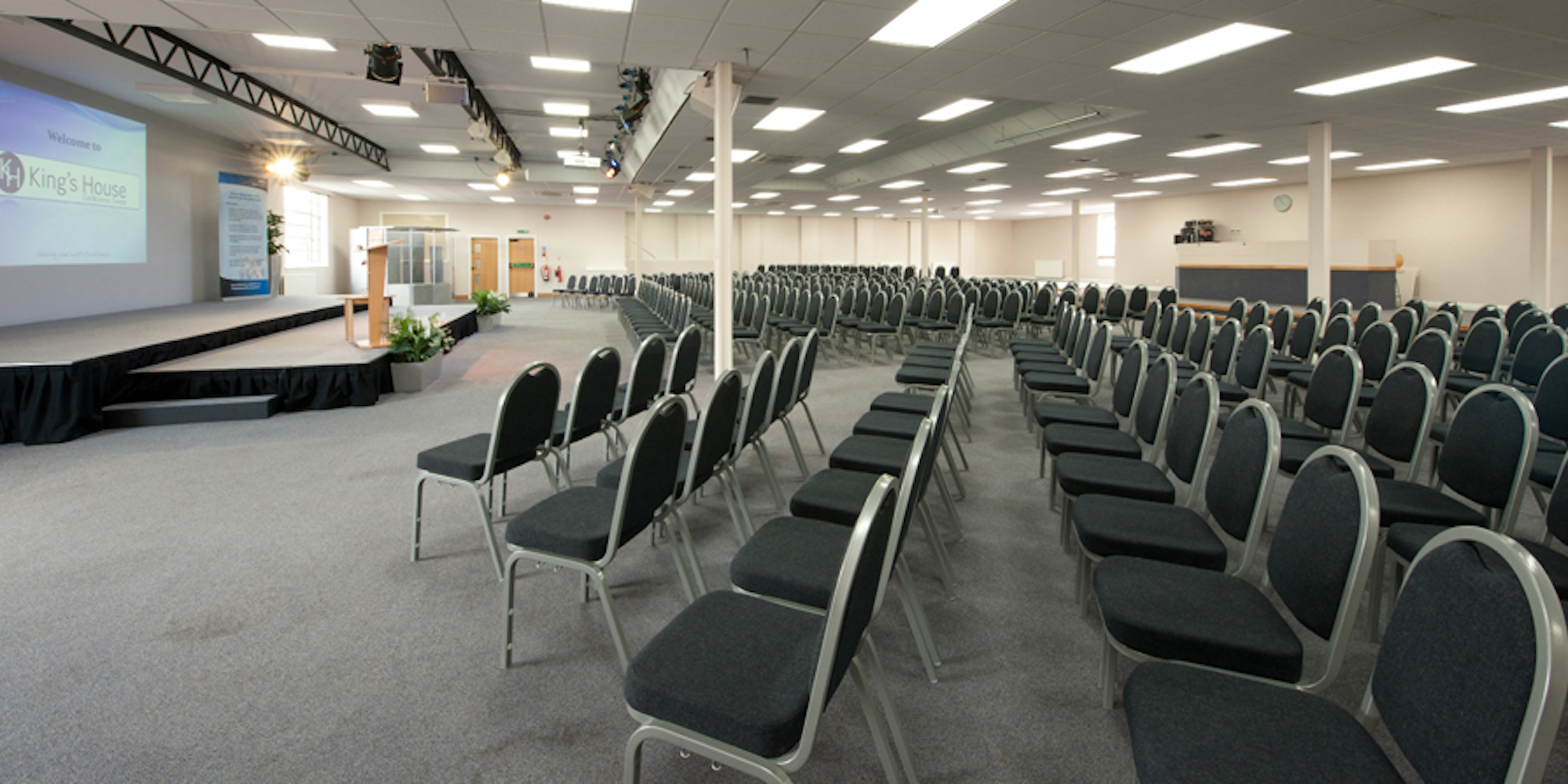 Spacious conference auditorium with empty chairs and stage at King's House Conference Centre.