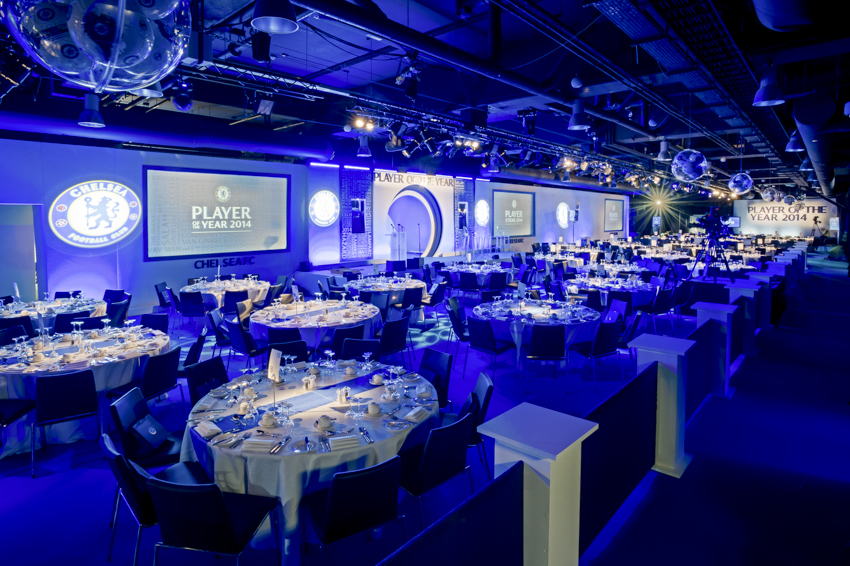 Great Hall at Chelsea FC set for formal dinner, featuring blue tablecloths and ambient lighting.