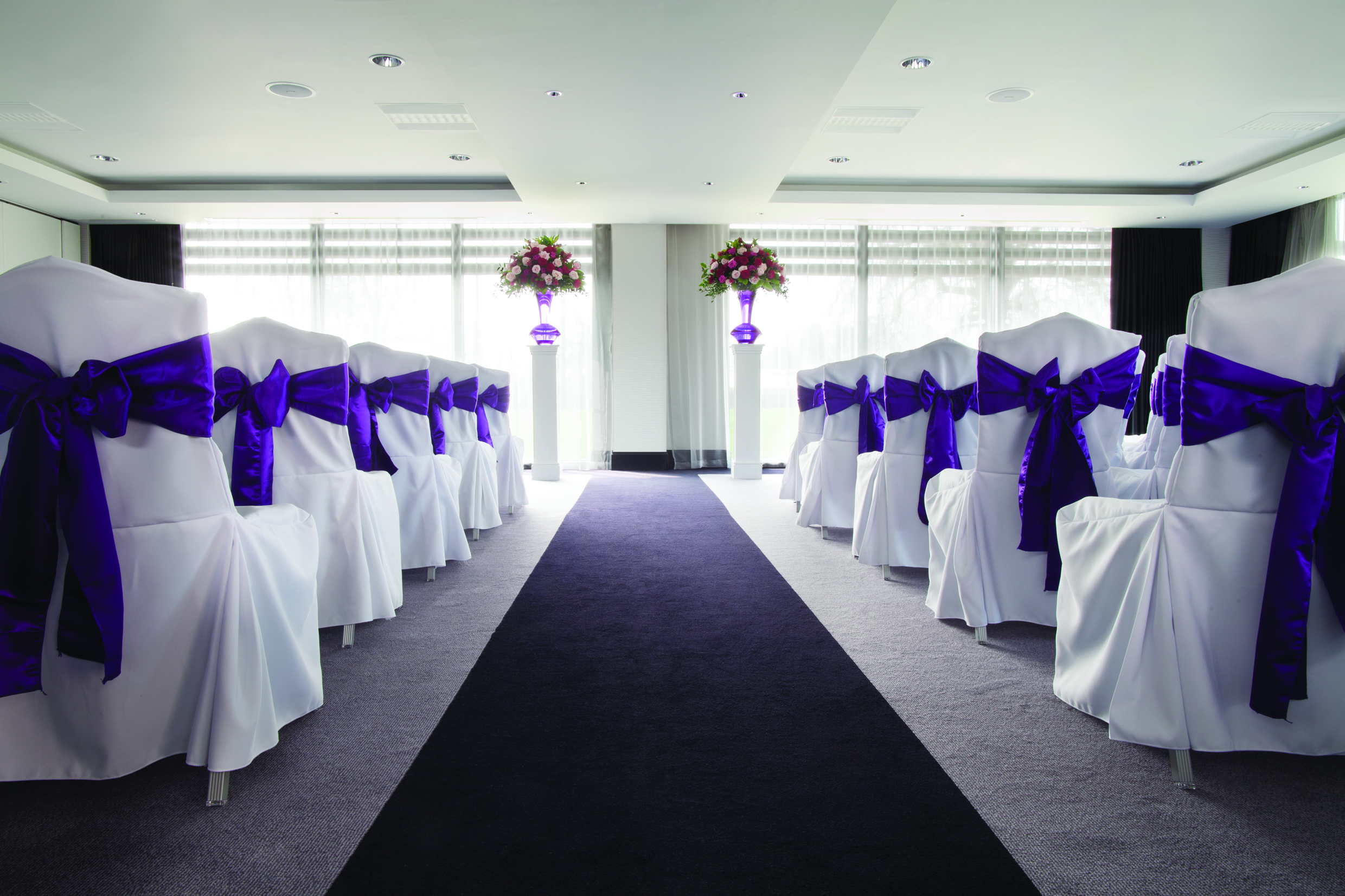 Elegant wedding venue at Hilton London Syon Park with white chairs and purple sashes.