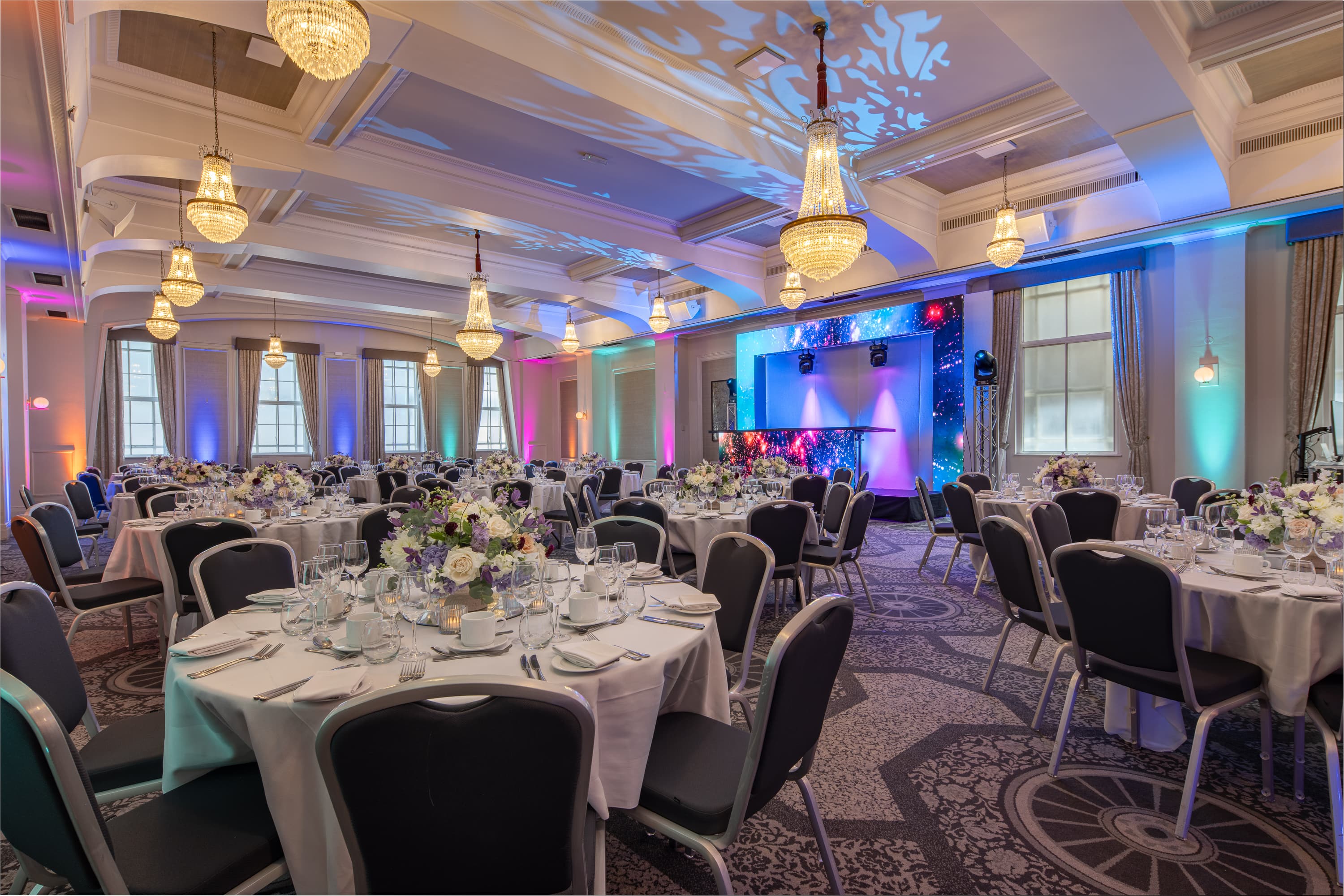 Elegant gala dinner setup in Grand Connaught Rooms with LED lighting and chandeliers.