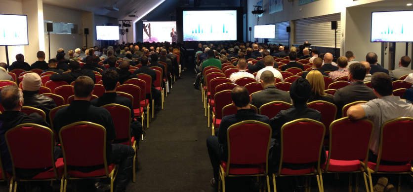 Conference at The Olympic Bar, StoneX Stadium with red chairs and large presentation screen.