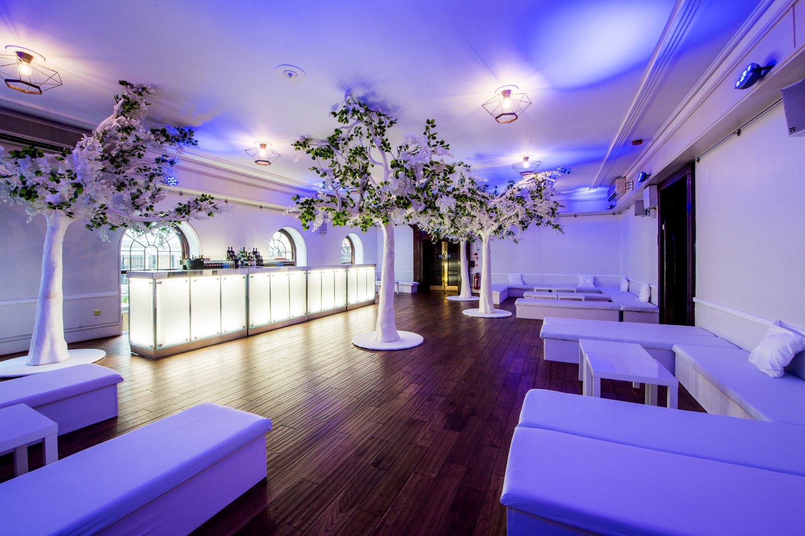 Elegant event space with white furniture and blue lighting, ideal for upscale gatherings.