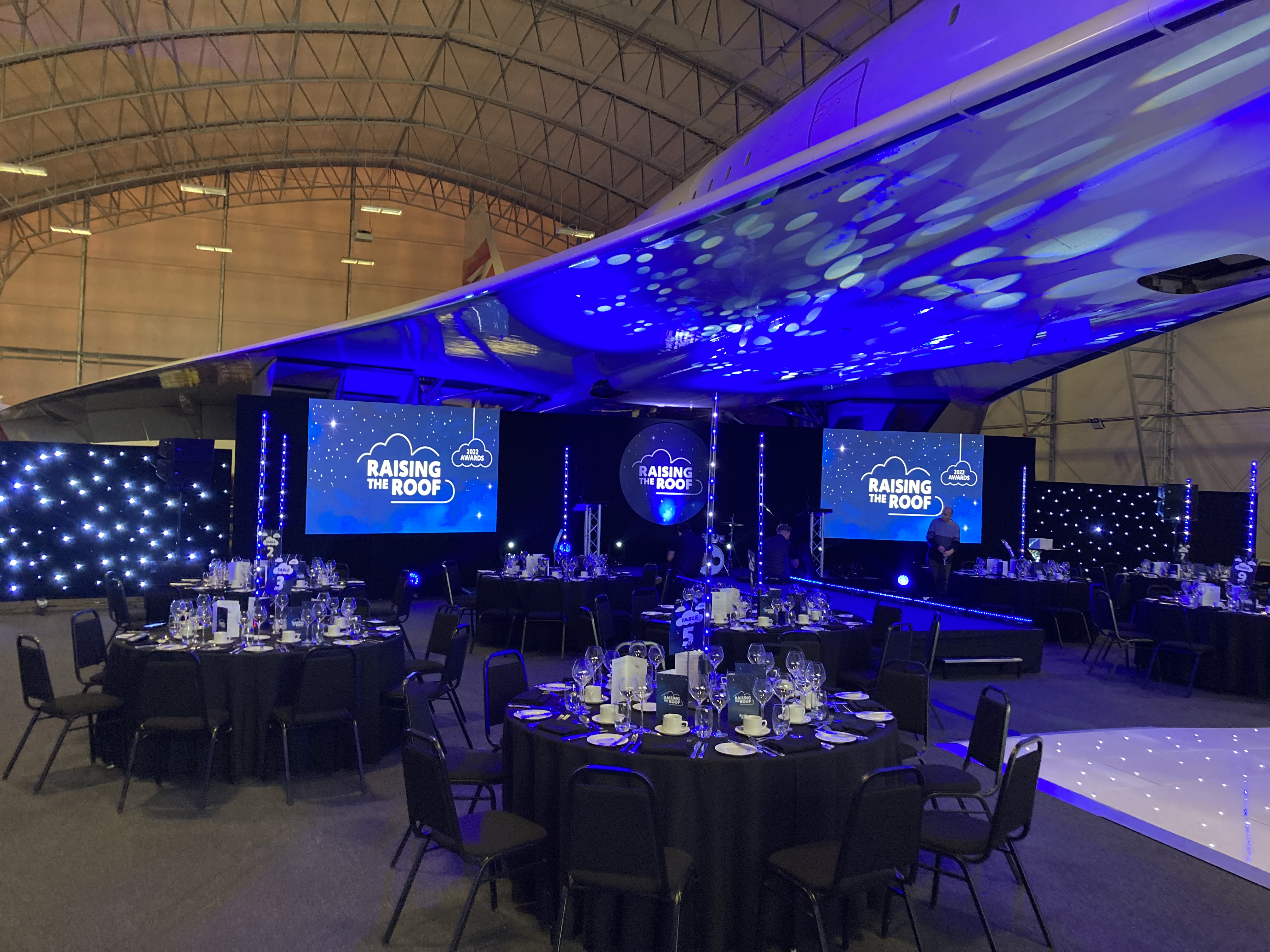 Concorde Hangar event setup with round tables, blue lighting for corporate functions.