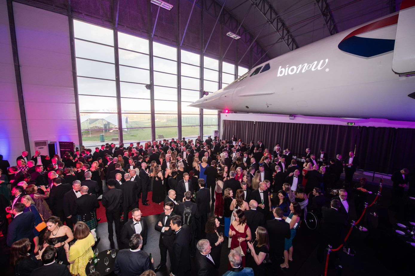 Gala event in Concorde Hangar with elegant attire and impressive aircraft backdrop.