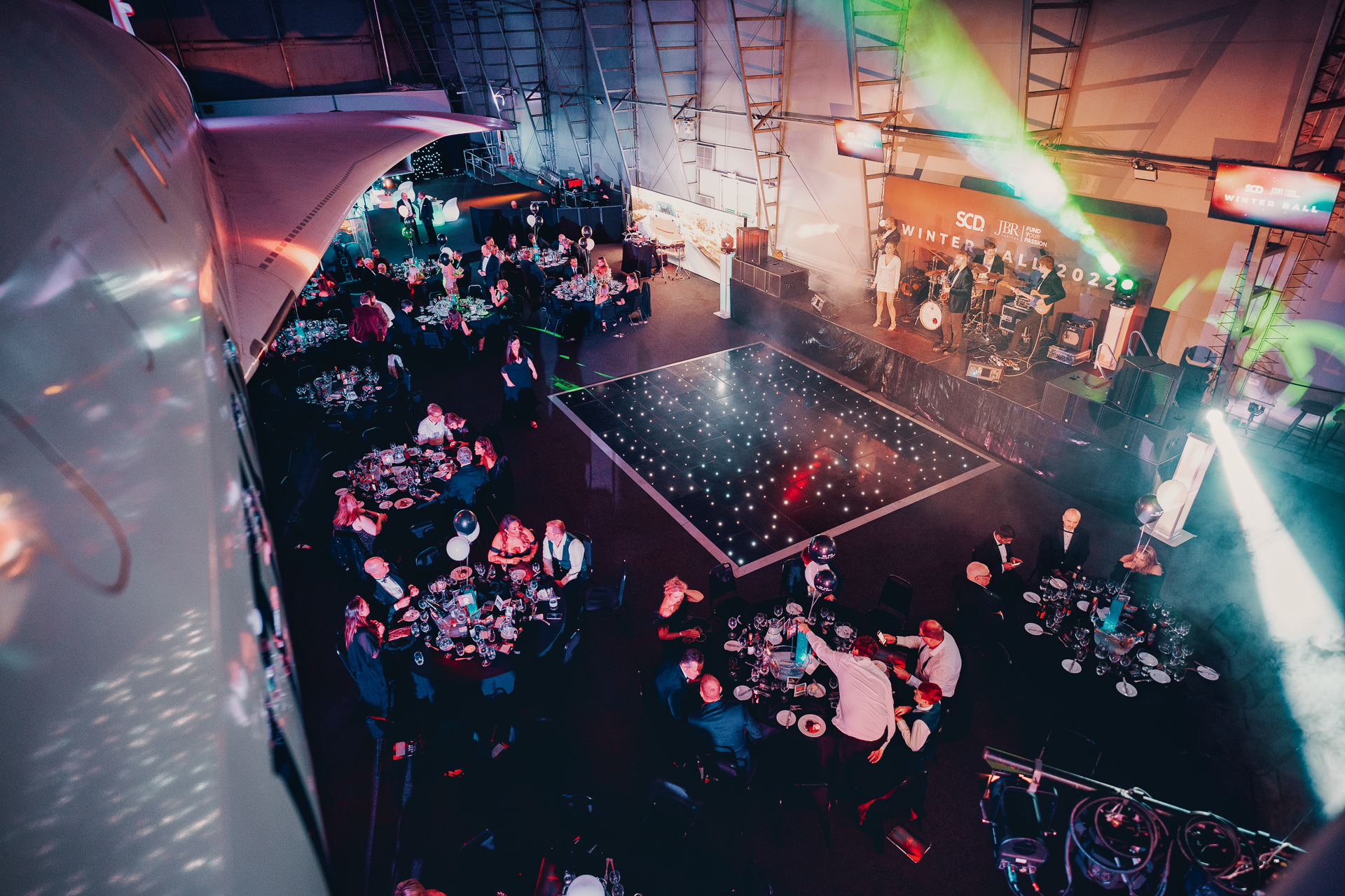 Concorde Hangar gala setup with elegant tables, dance floor, and stage for corporate events.