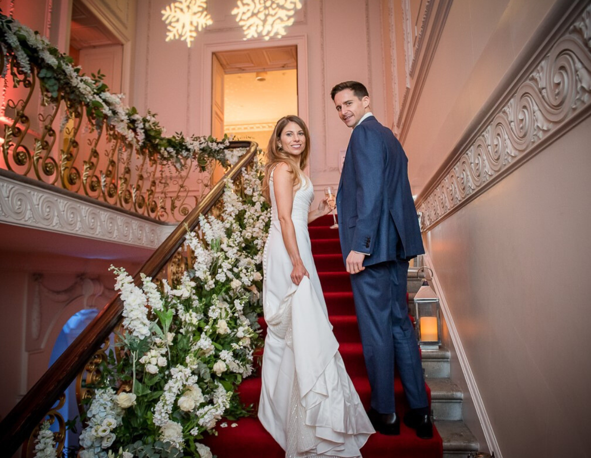Elegant wedding scene on staircase at Kent House Knightsbridge, adorned with flowers.