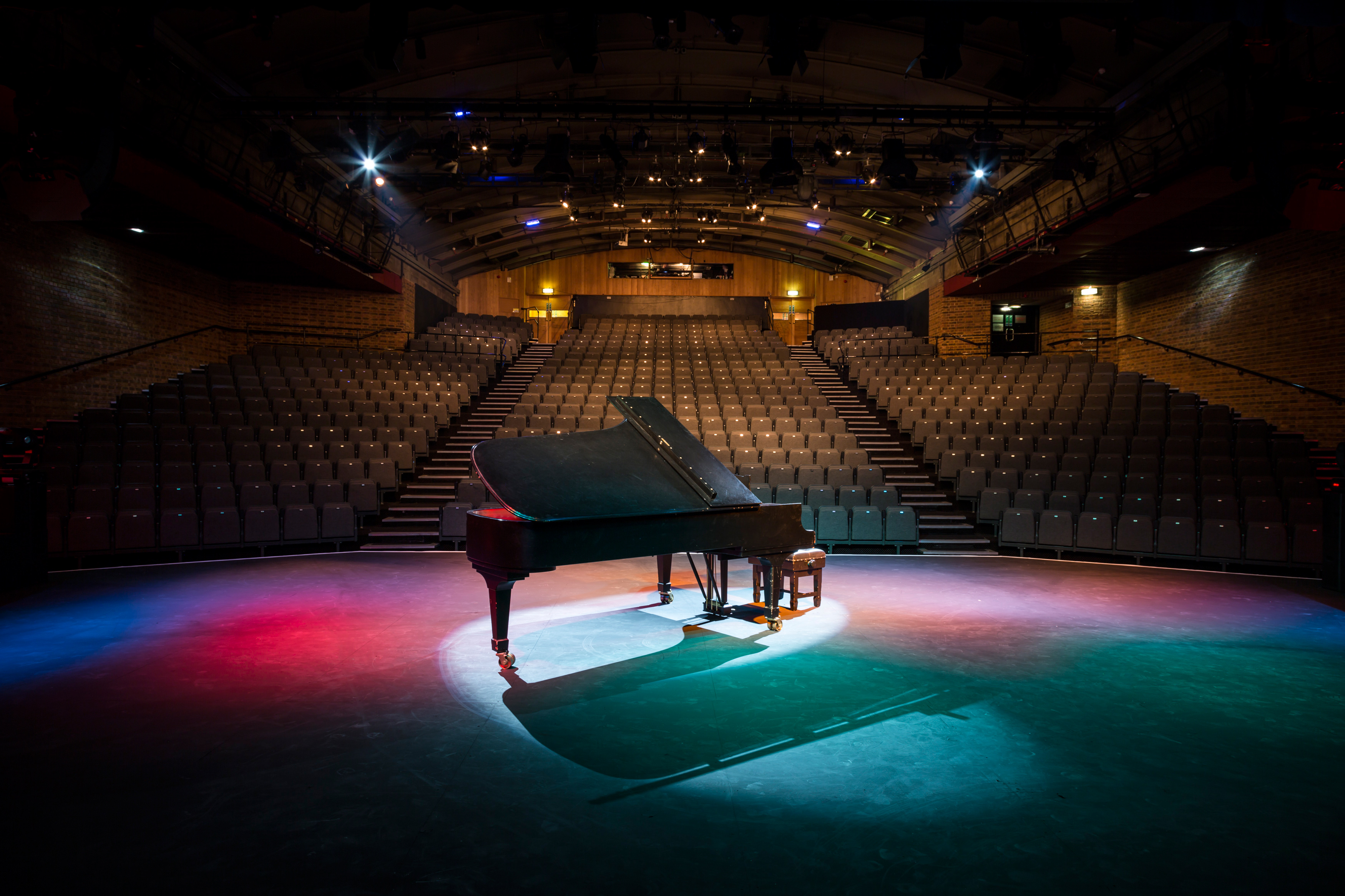 Grand piano on stage in empty Mermaid London auditorium, perfect for intimate events.
