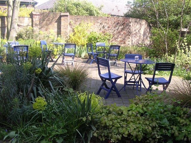 Charming outdoor networking space with blue furniture and lush greenery at Estorick Collection.