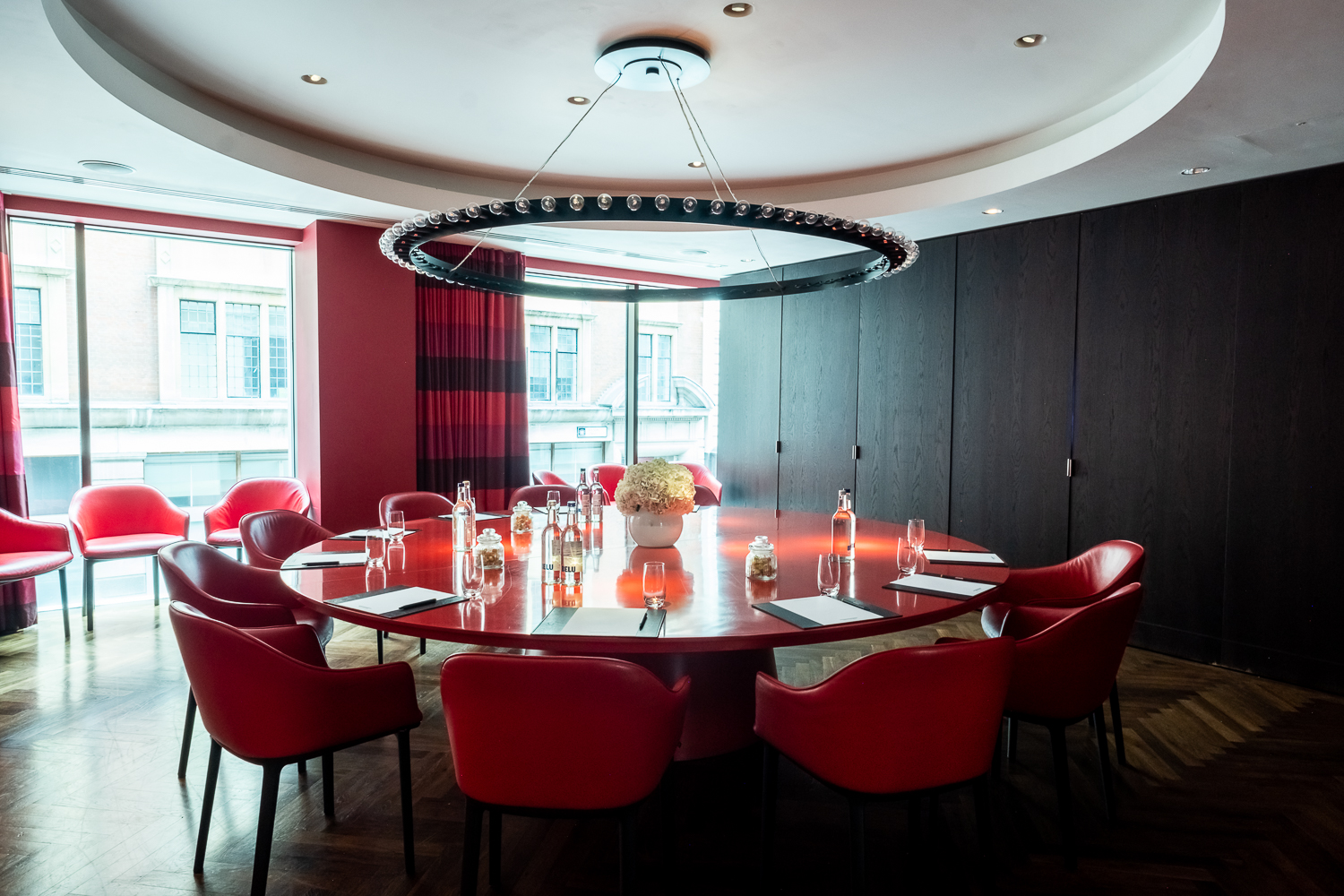 Modern meeting room at South Place Hotel with round table and vibrant red chairs.