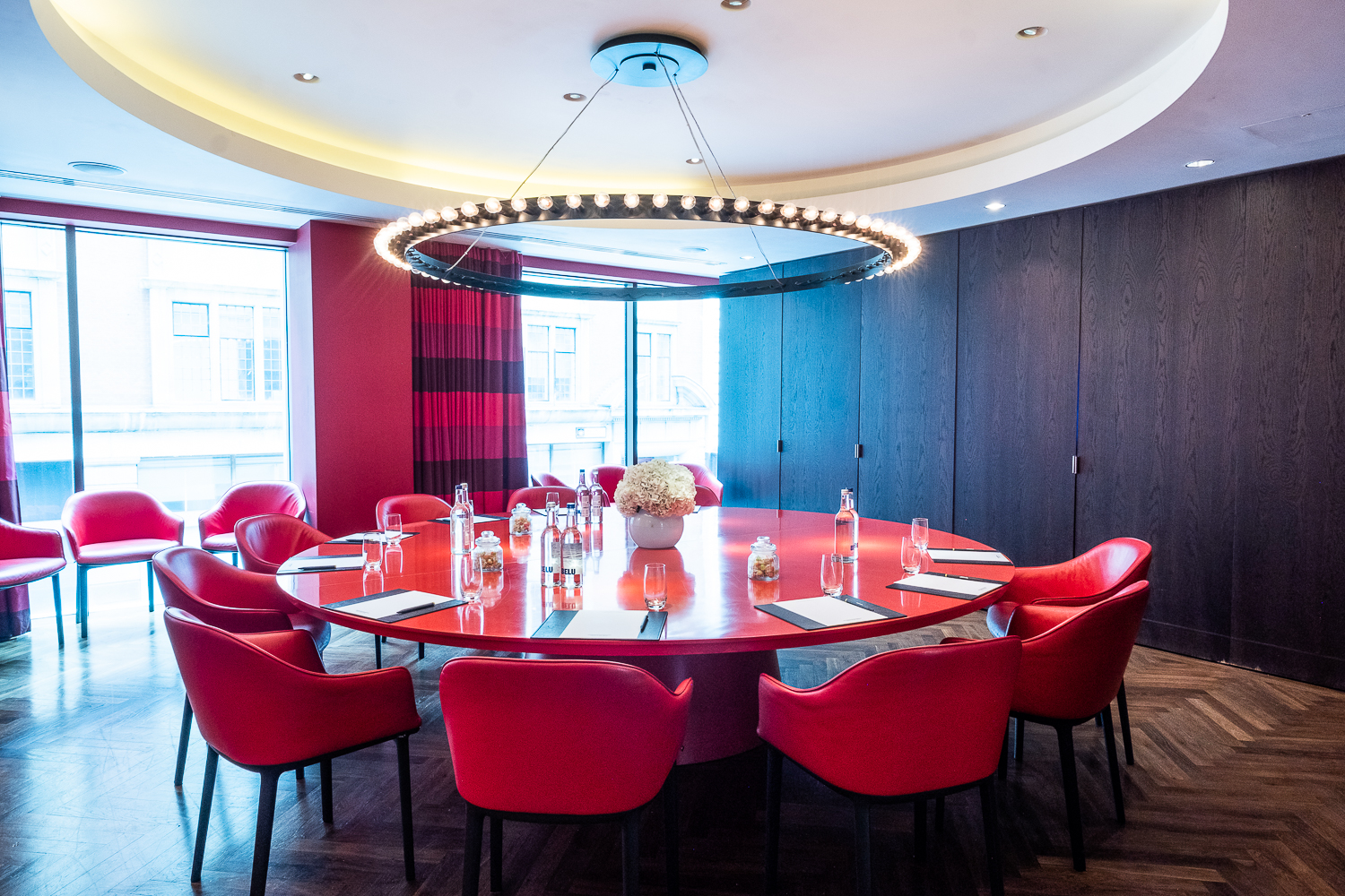 Modern meeting room at South Place Hotel with round table and vibrant red chairs.