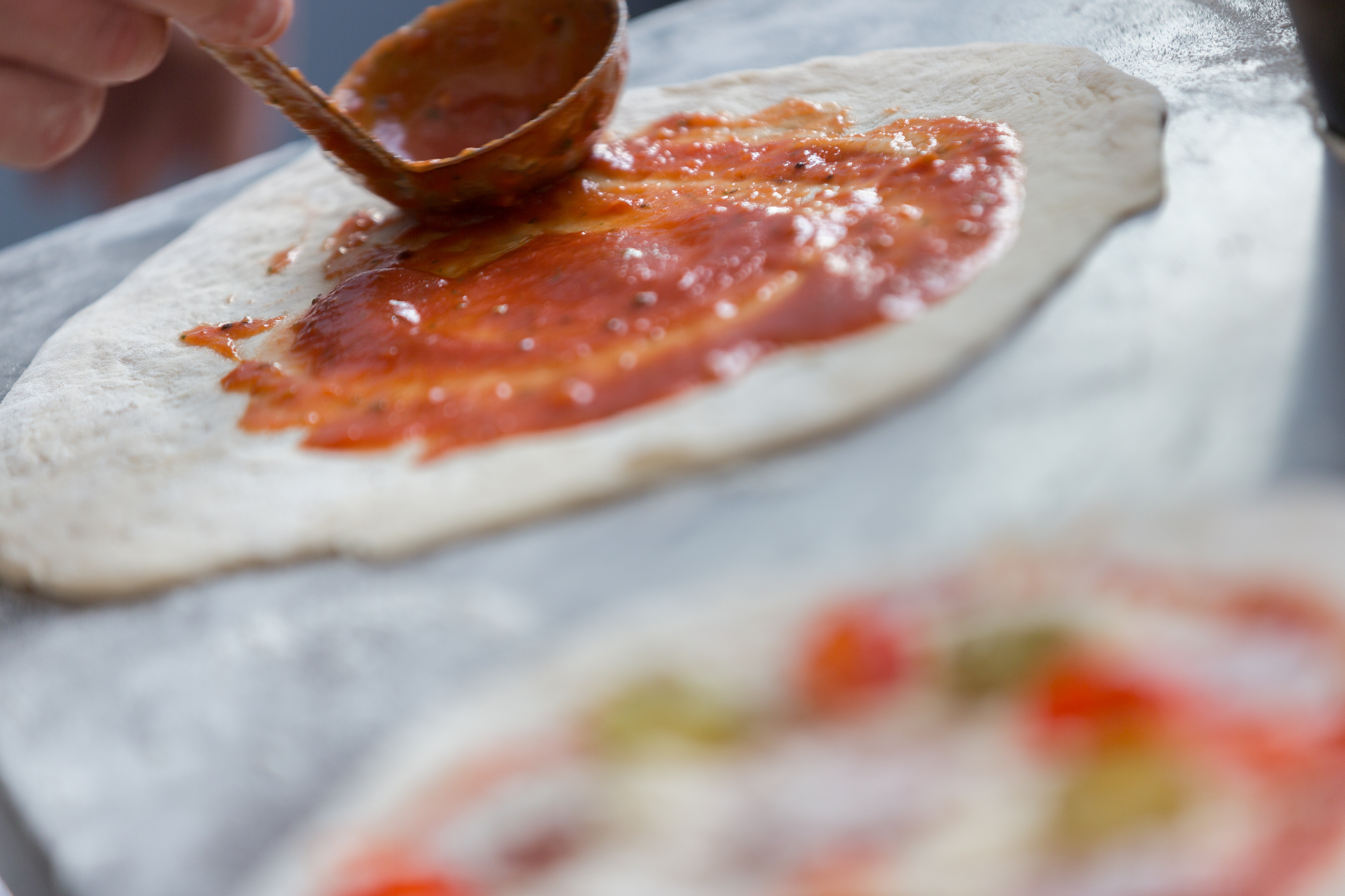 Pizza-making process at Hotel Football, showcasing sauce application for team-building events.