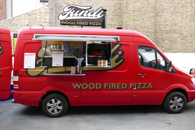 Vibrant red food truck serving wood-fired pizza at outdoor events in Shoreditch Studios.
