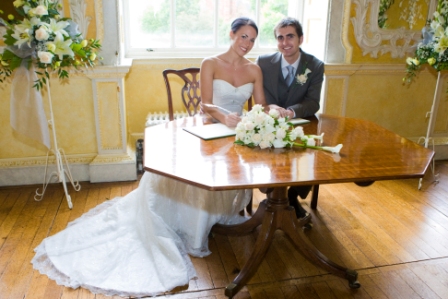 Couple at wedding ceremony in The Saloon, Hagley Hall, with floral centerpiece.
