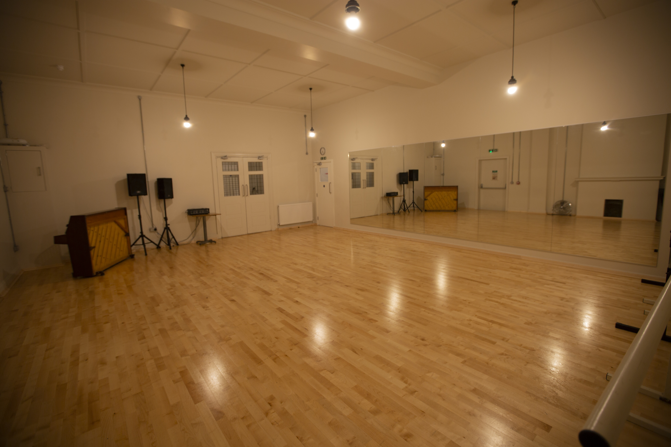 Versatile event space with polished wooden floors and large mirror for workshops and dance classes.