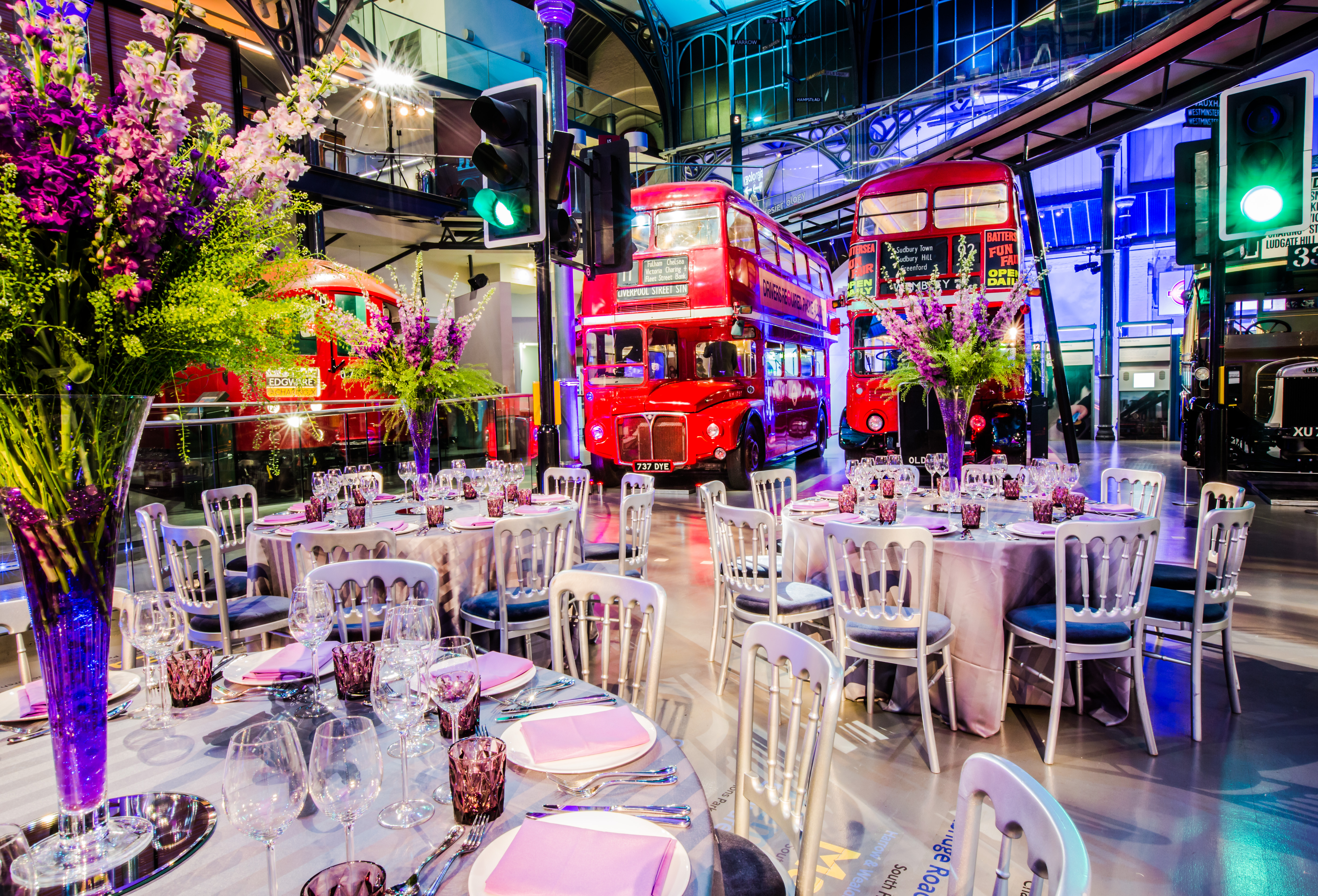 Elegant event space in London Transport Museum with floral centerpieces and red buses.