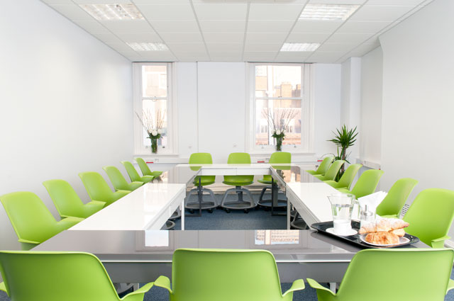 Modern meeting room with U-shaped layout and green chairs, perfect for workshops.