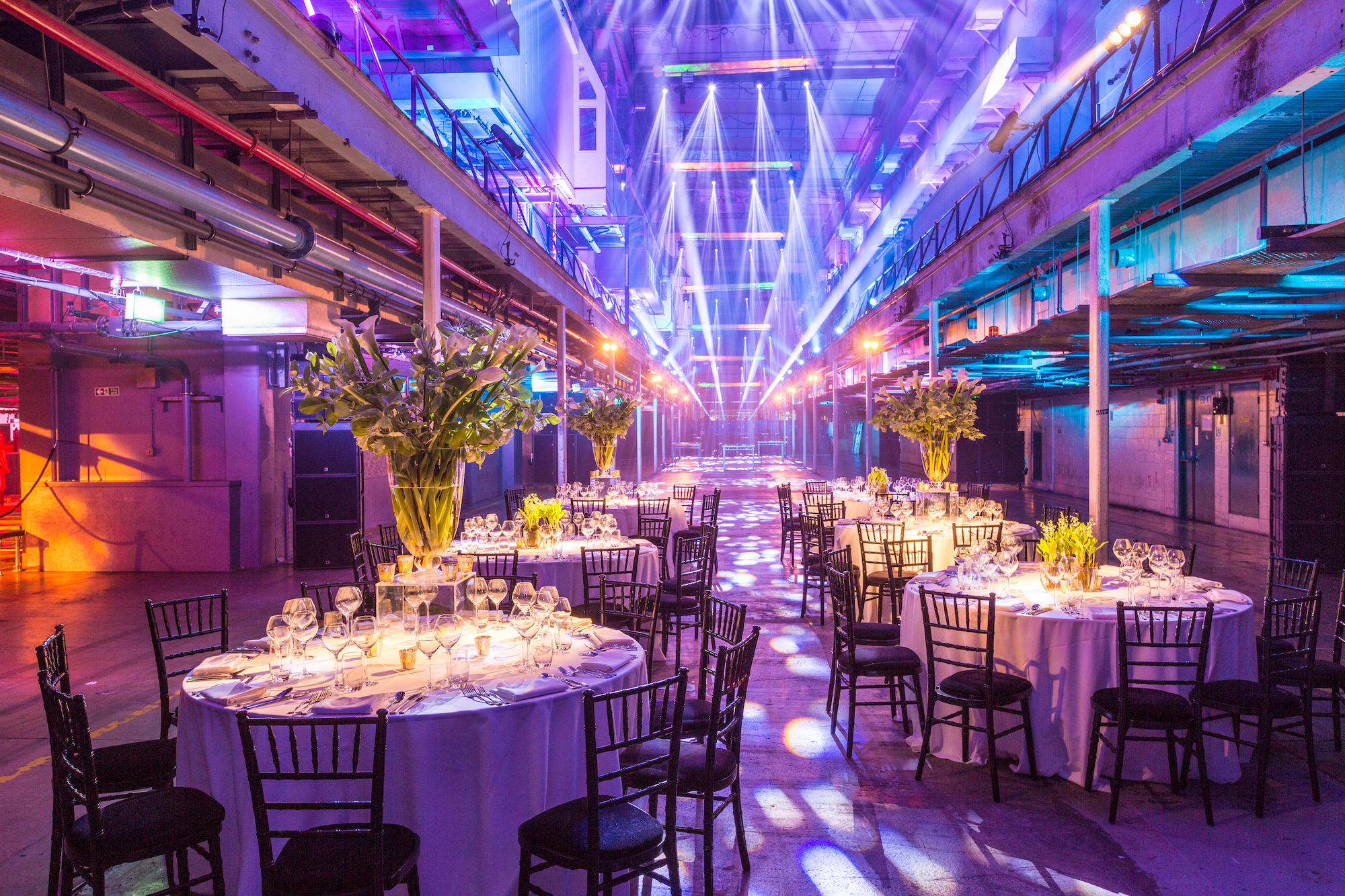 Gala dinner setup in The Press Halls, Printworks London with floral centerpieces.