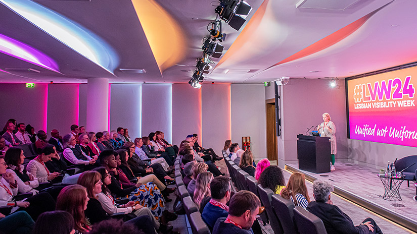 Lesbian visibility conference at London Stock Exchange with engaged audience and vibrant lighting.