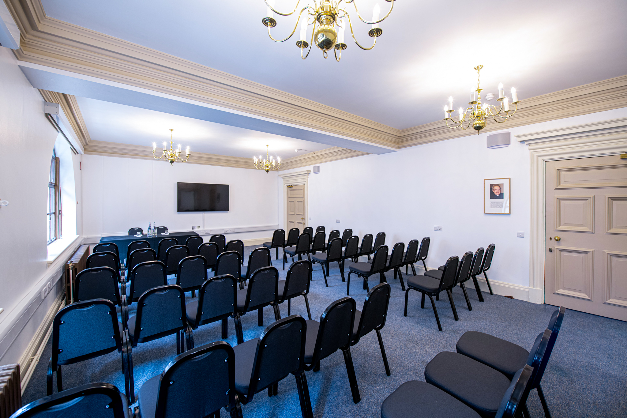 John Tudor presenting in a well-lit seminar room with black chairs and screen.