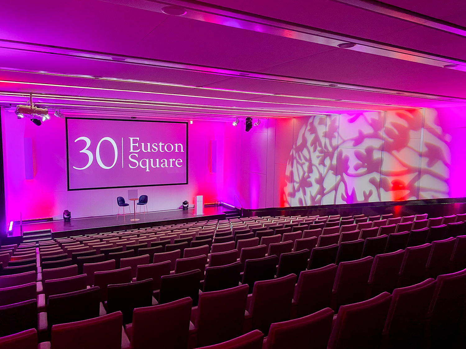 Modern auditorium with tiered seating and pink lighting for corporate events at 30 Euston Square.