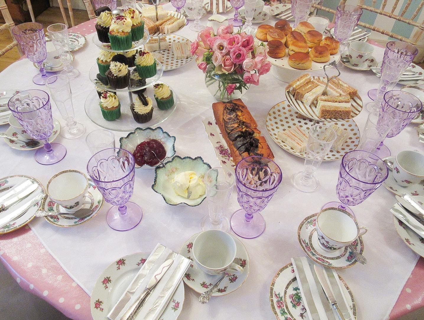 Elegant tea party table with desserts and floral centerpieces in pastel colors.