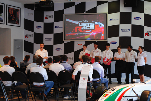 Corporate event at Let's Race with attendees focused on motorsports presentation.