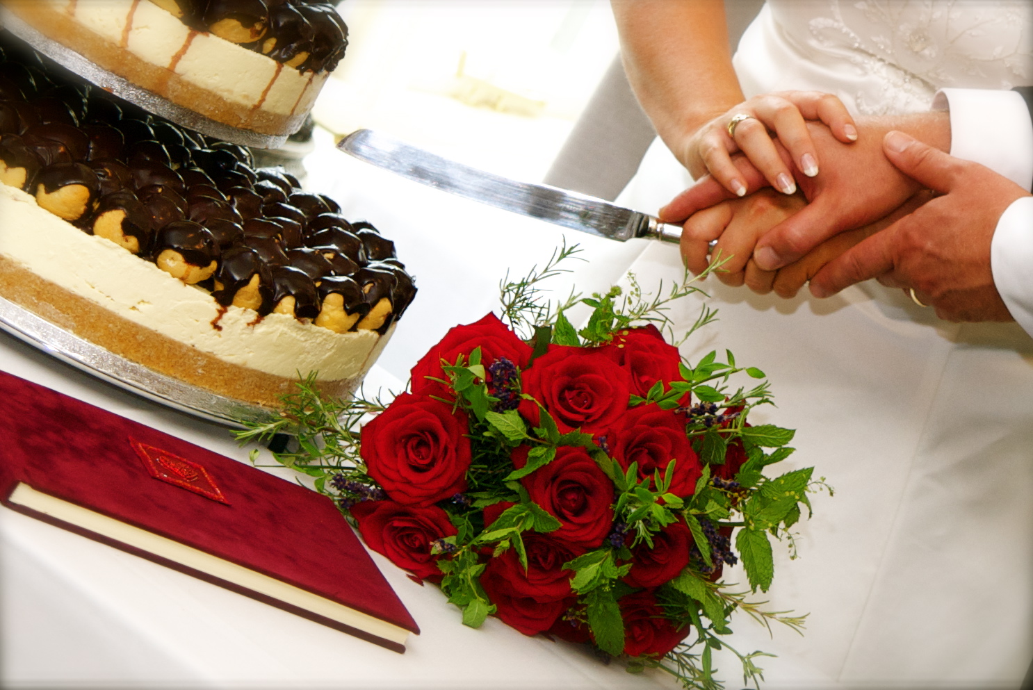 Bournville Suite wedding scene with couple's hands, red roses, and elegant cake.