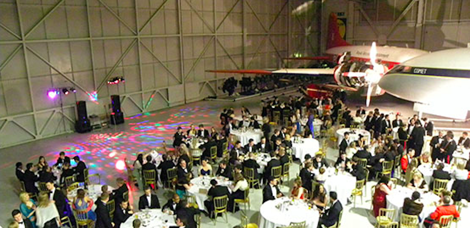 Gala event in RAF Museum's Hangar One with elegant guests and vintage airplane backdrop.