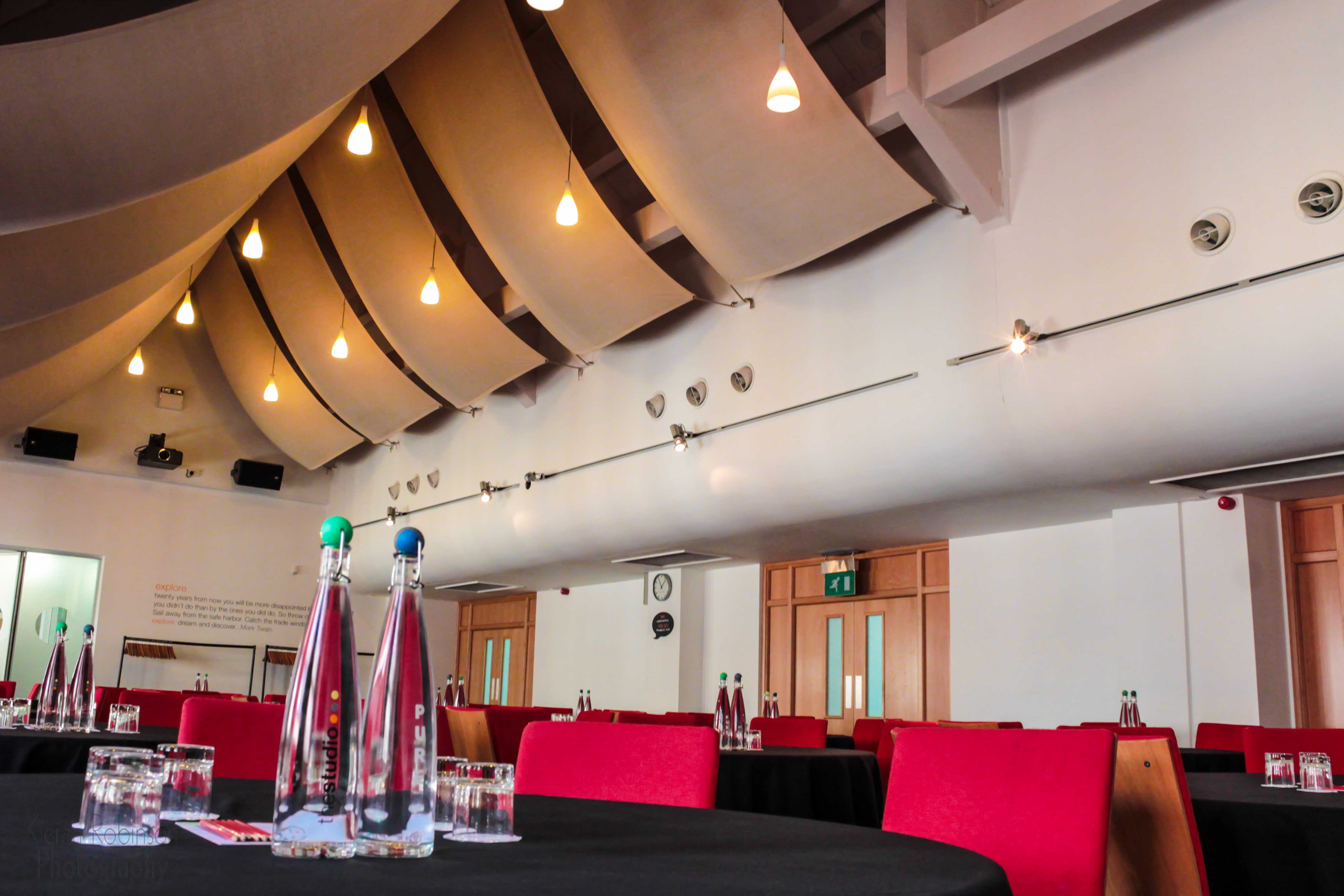 Modern event space in Birmingham with round tables and vibrant red chairs for meetings.