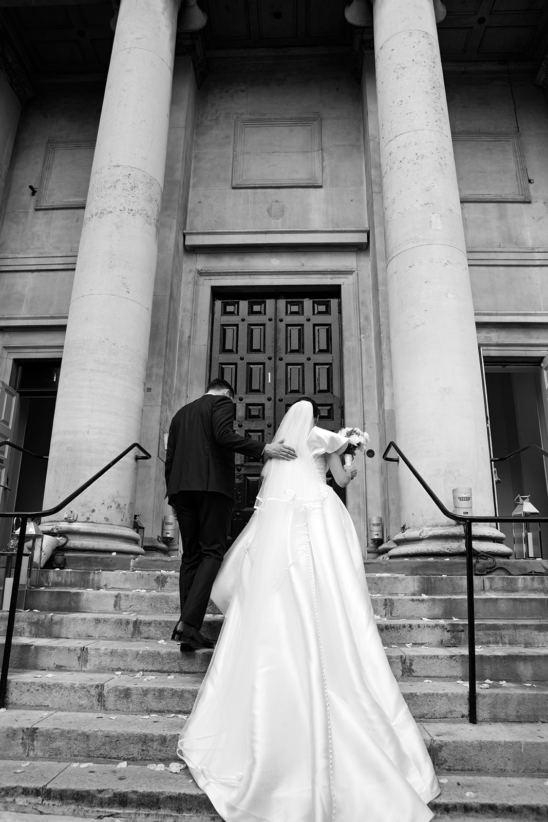 Couple in formal attire ascending steps of Soane Hall for a wedding ceremony.