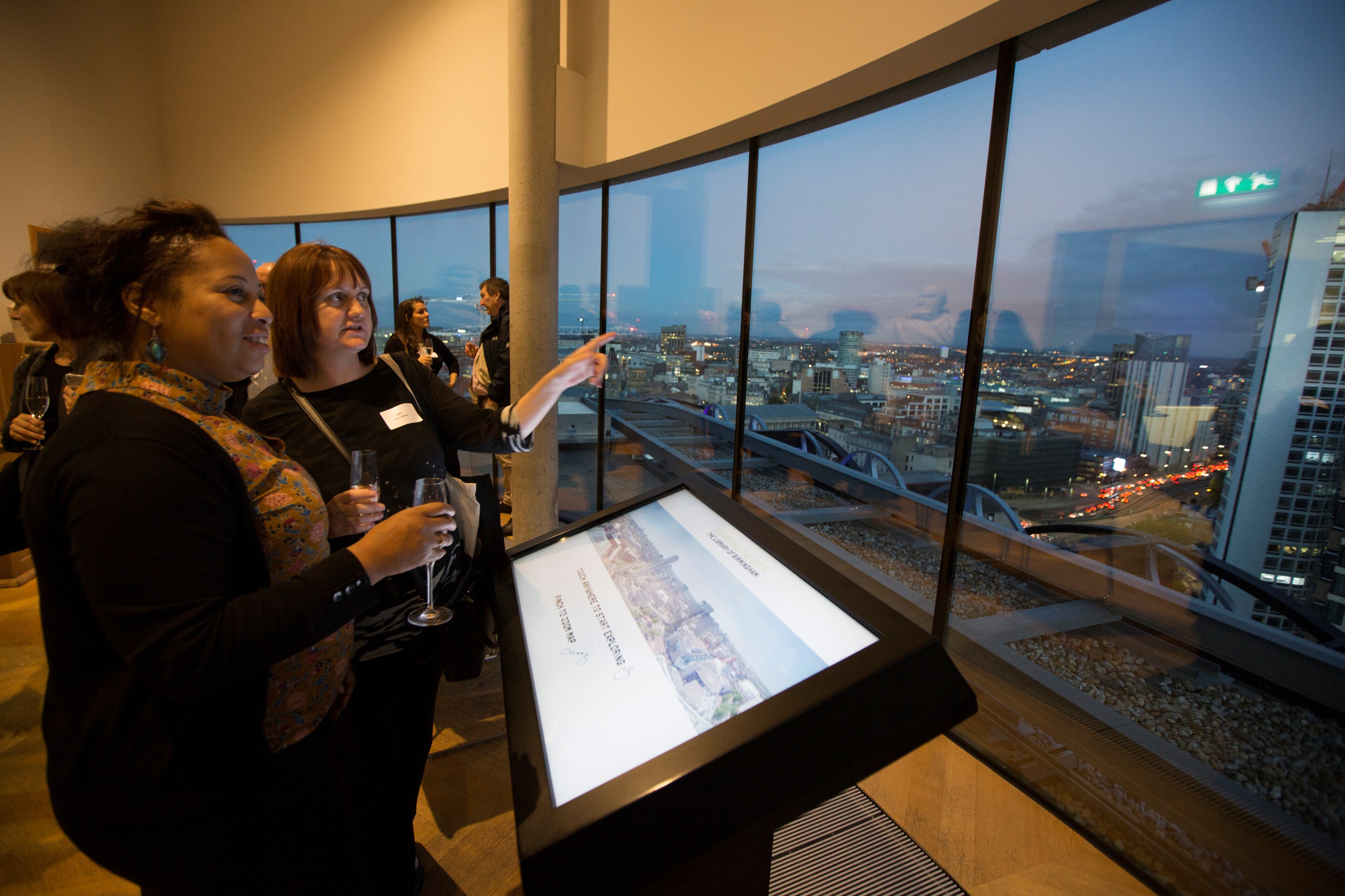 Attendees networking in Shakespeare Memorial Room with city view and digital display.