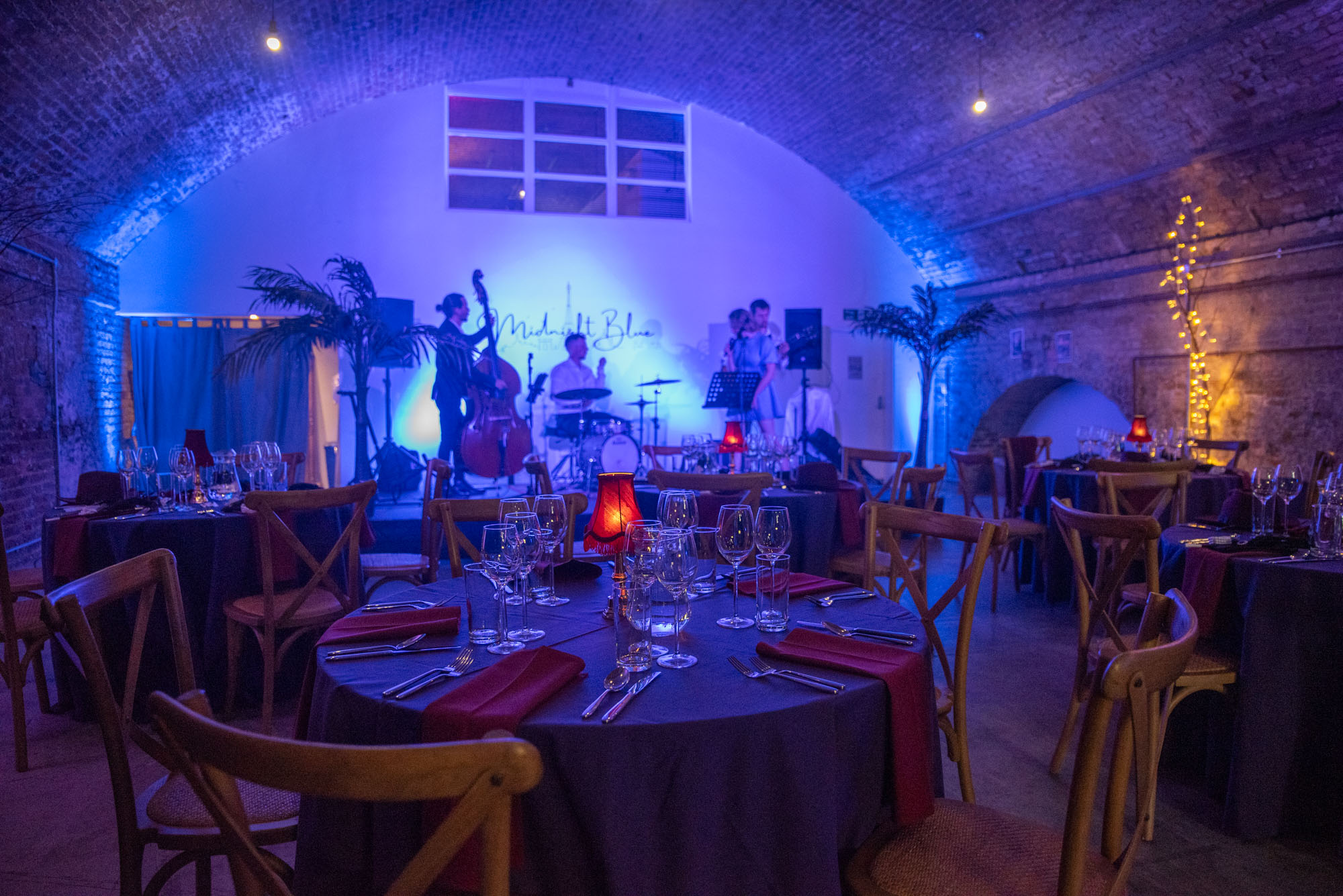 Elegant event space with round tables, deep red napkins, and live band for upscale gatherings.