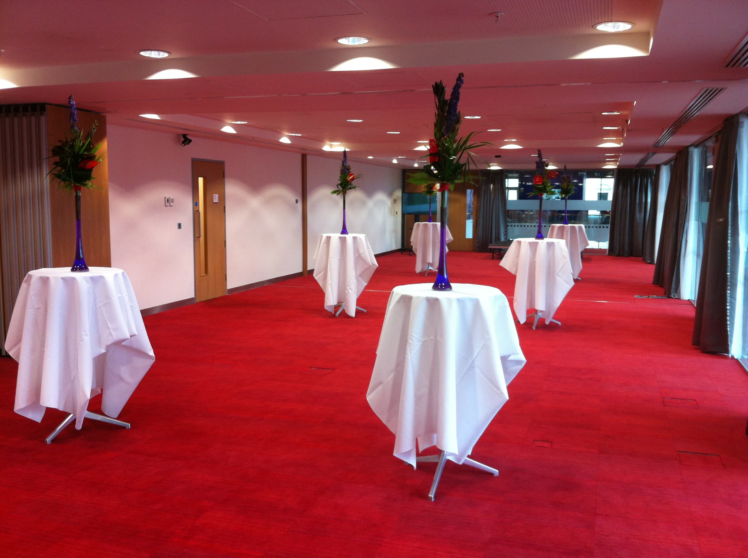 Spacious event room with high-top tables and floral centerpieces for networking receptions.