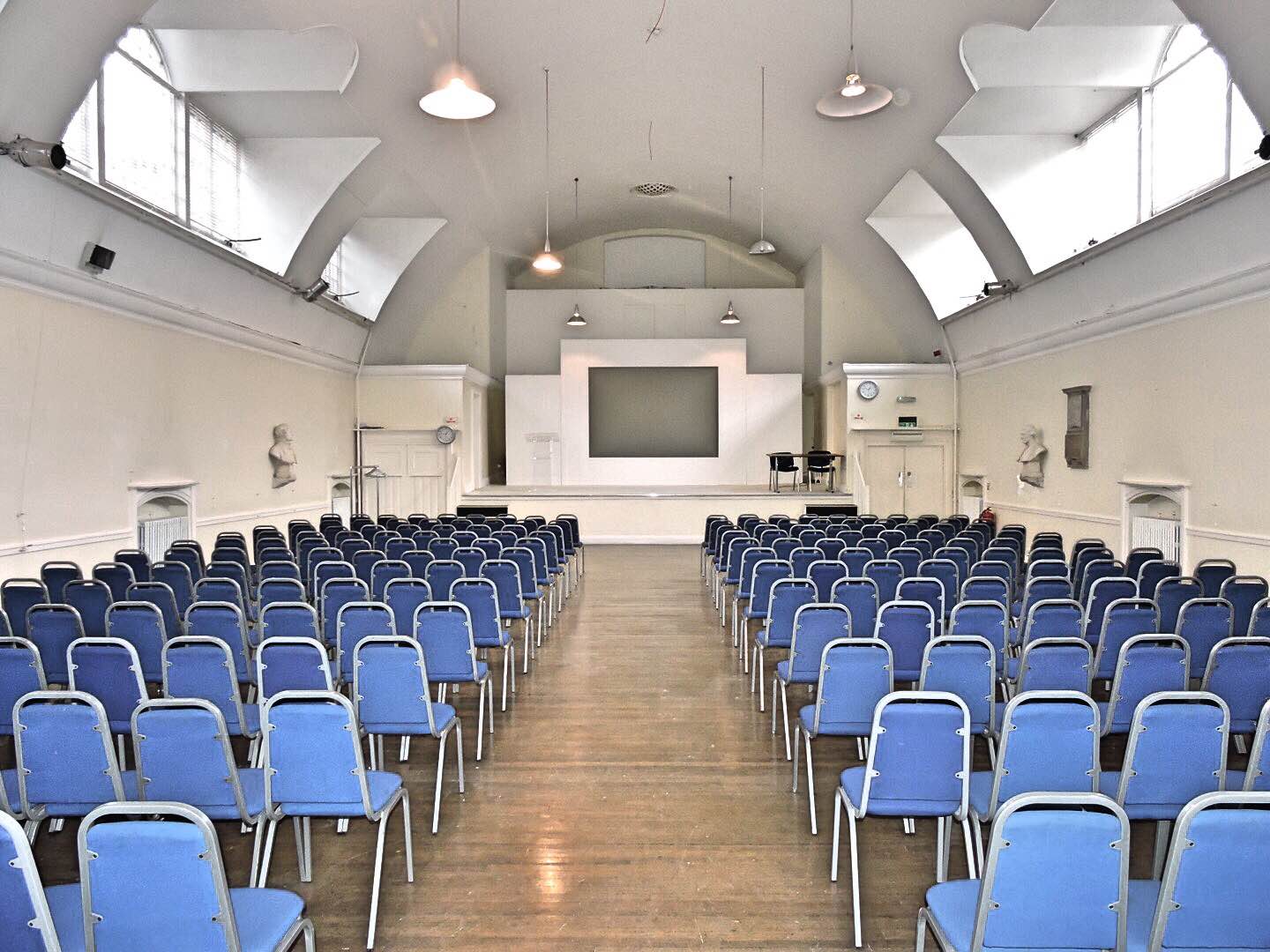 Mary Ward Hall conference venue with blue chairs and large screen, ideal for events.