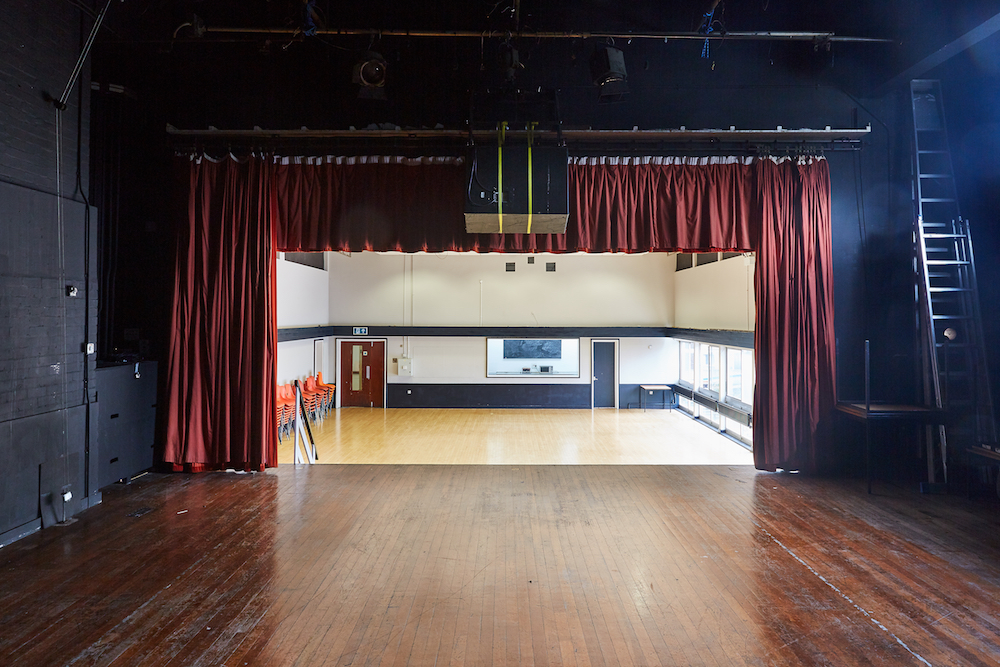 Main Hall at Mill Co. Rose Lipman, featuring a stage and elegant red curtains for events.