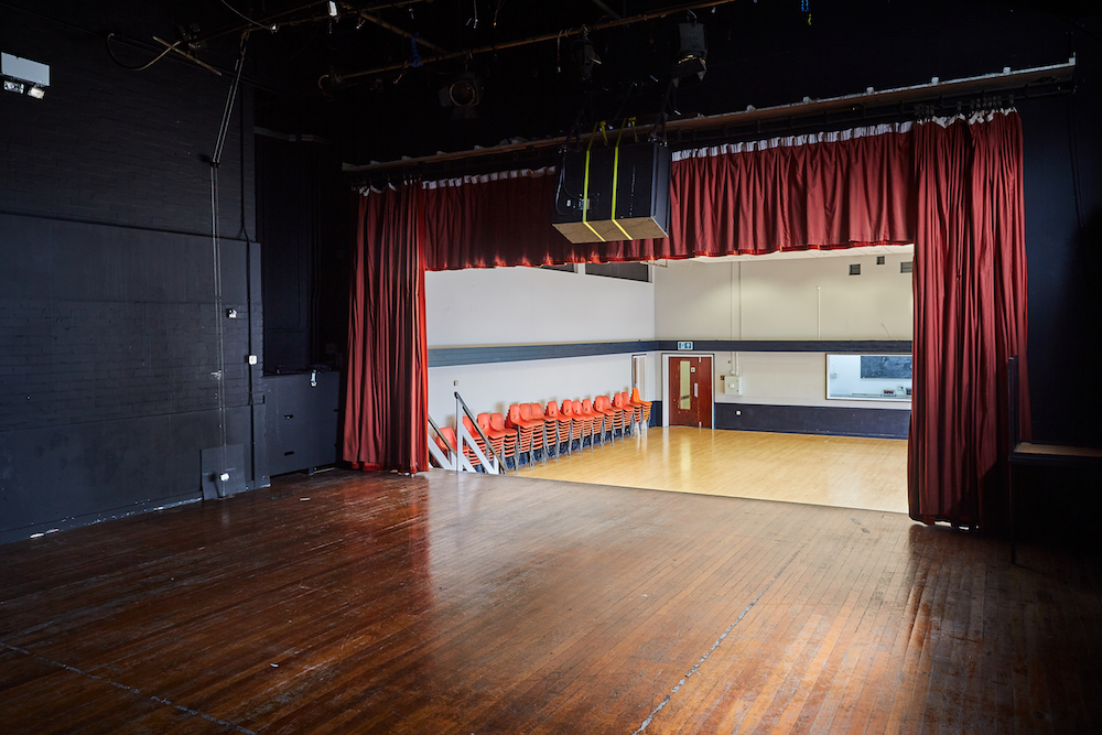 Main Hall at Mill Co. Rose Lipman, versatile event space with stage and red curtains.
