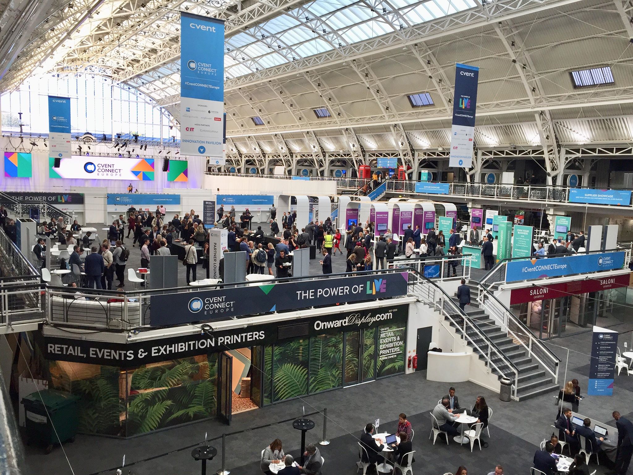 Mezzanine exhibition hall with high ceilings, vibrant networking event atmosphere.