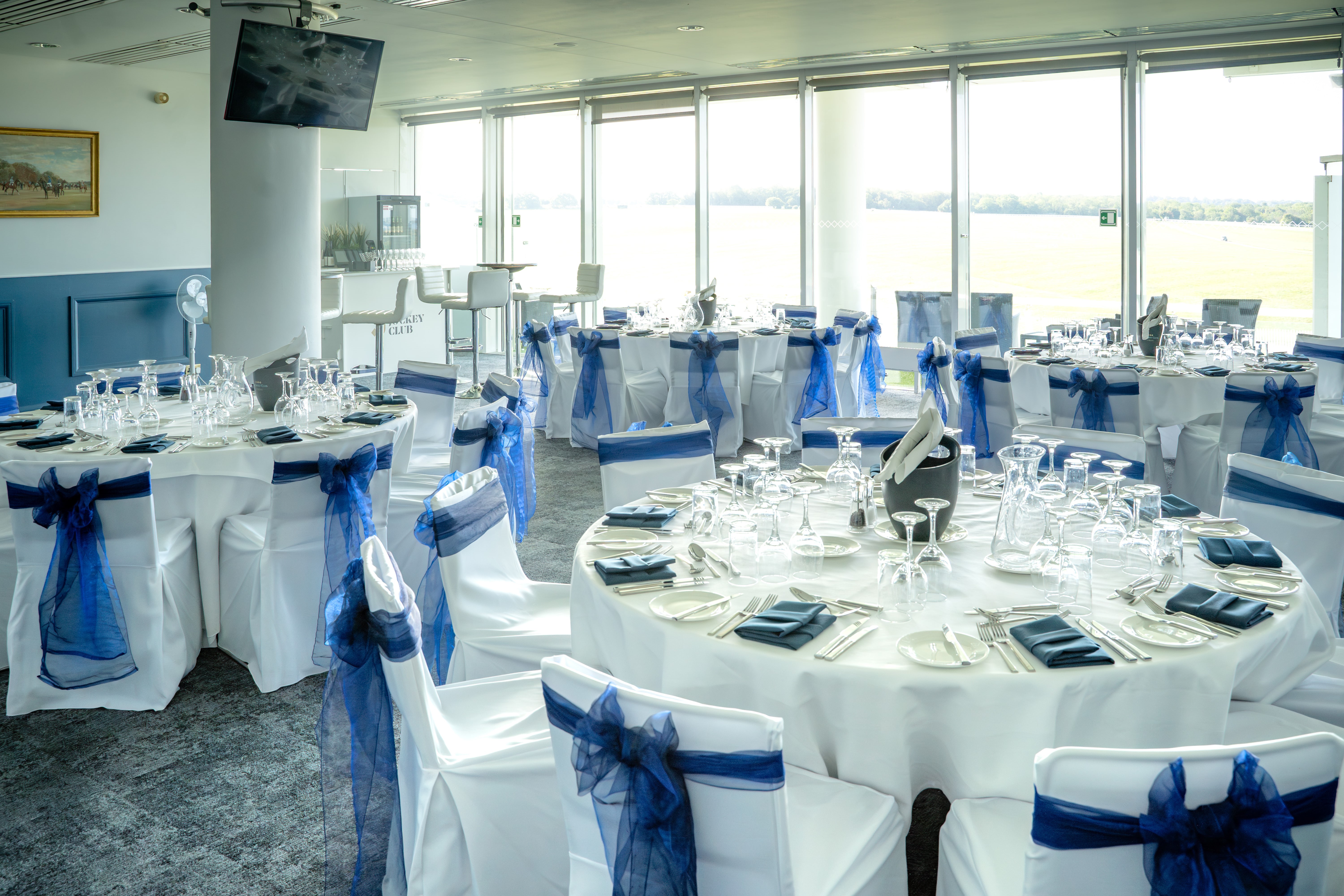Elegant event space at Epsom Downs Racecourse with blue sashes and panoramic windows.